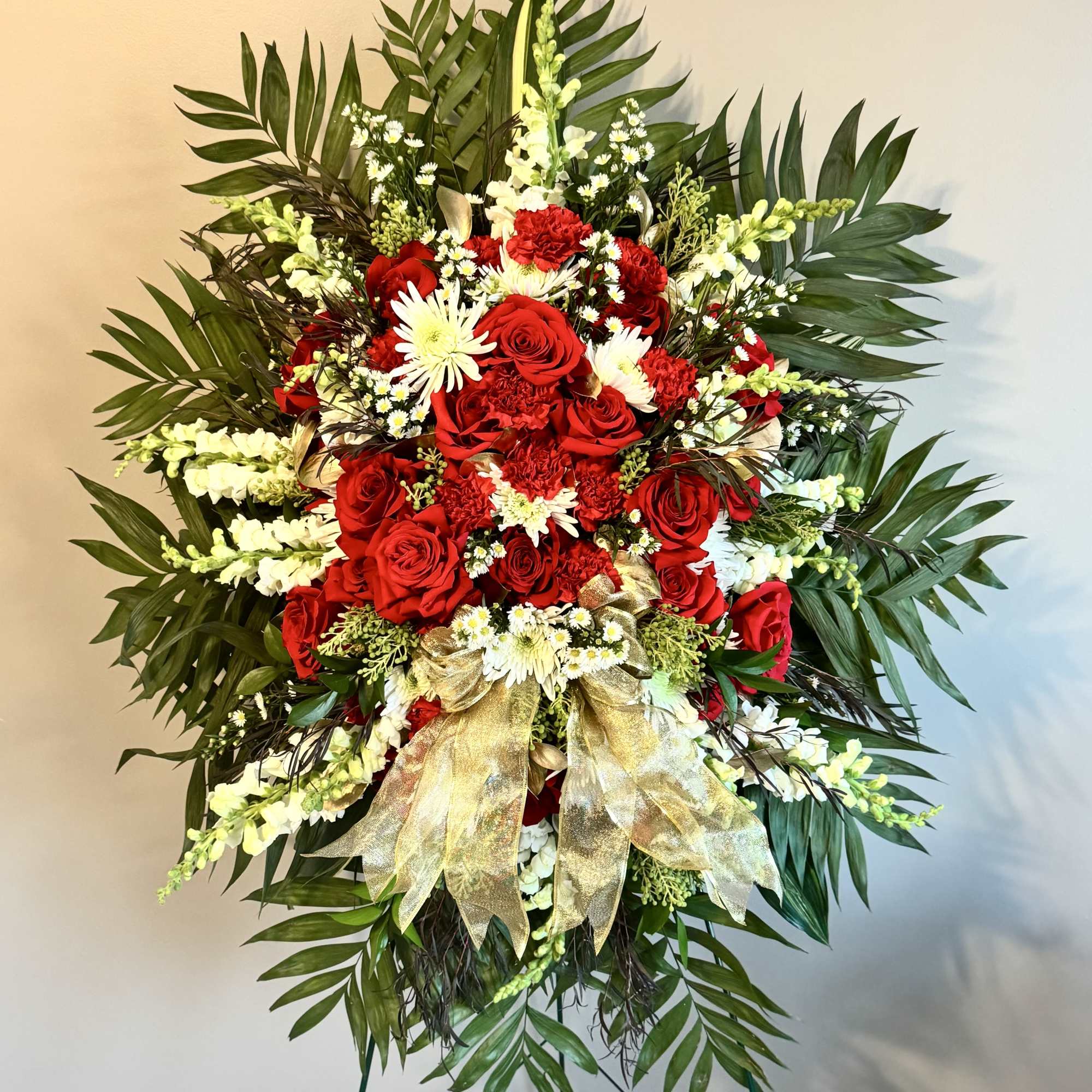Standing floral spray with red roses and white flowers on a gold ribboned easel