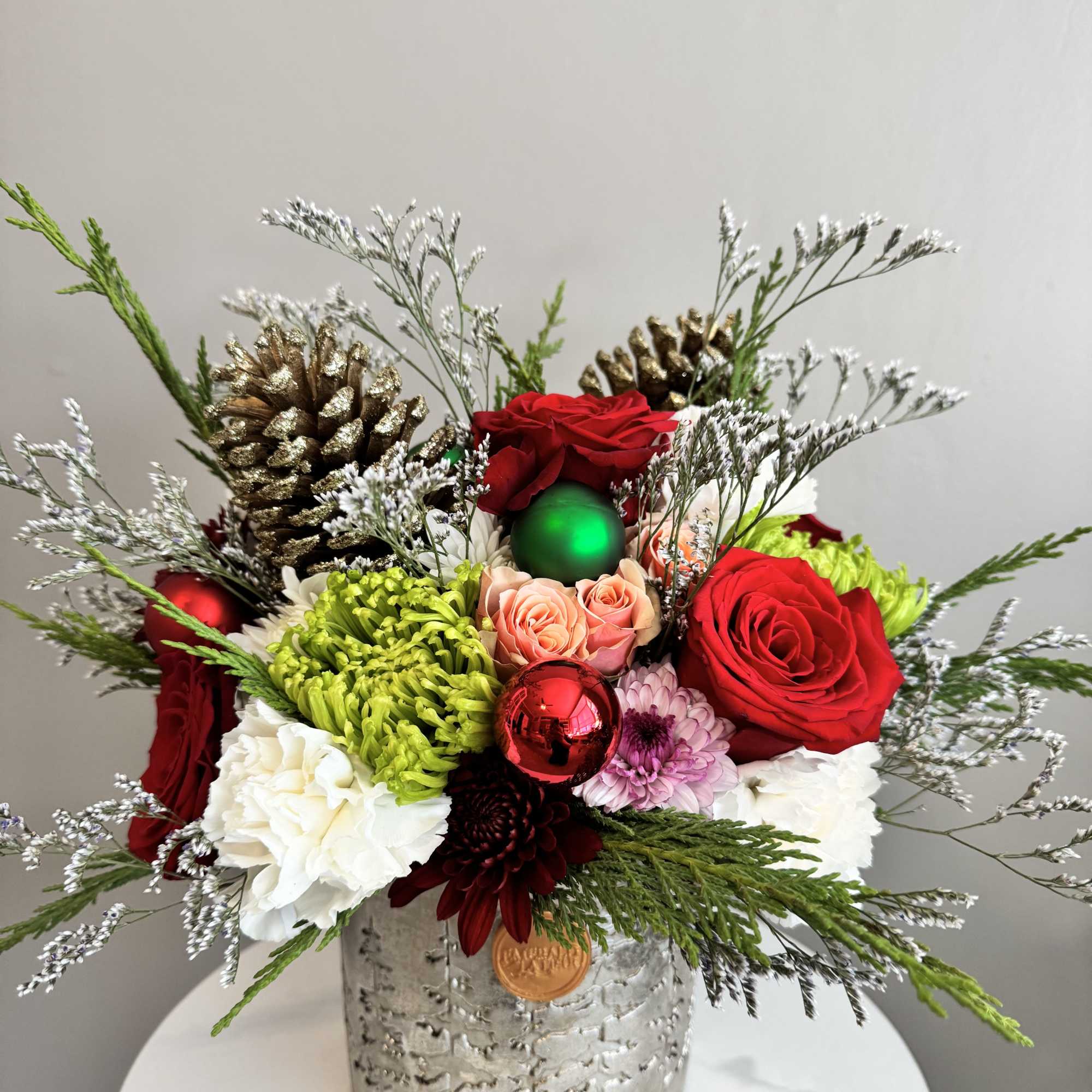 Holiday floral arrangement in a silver container with red roses and ornaments