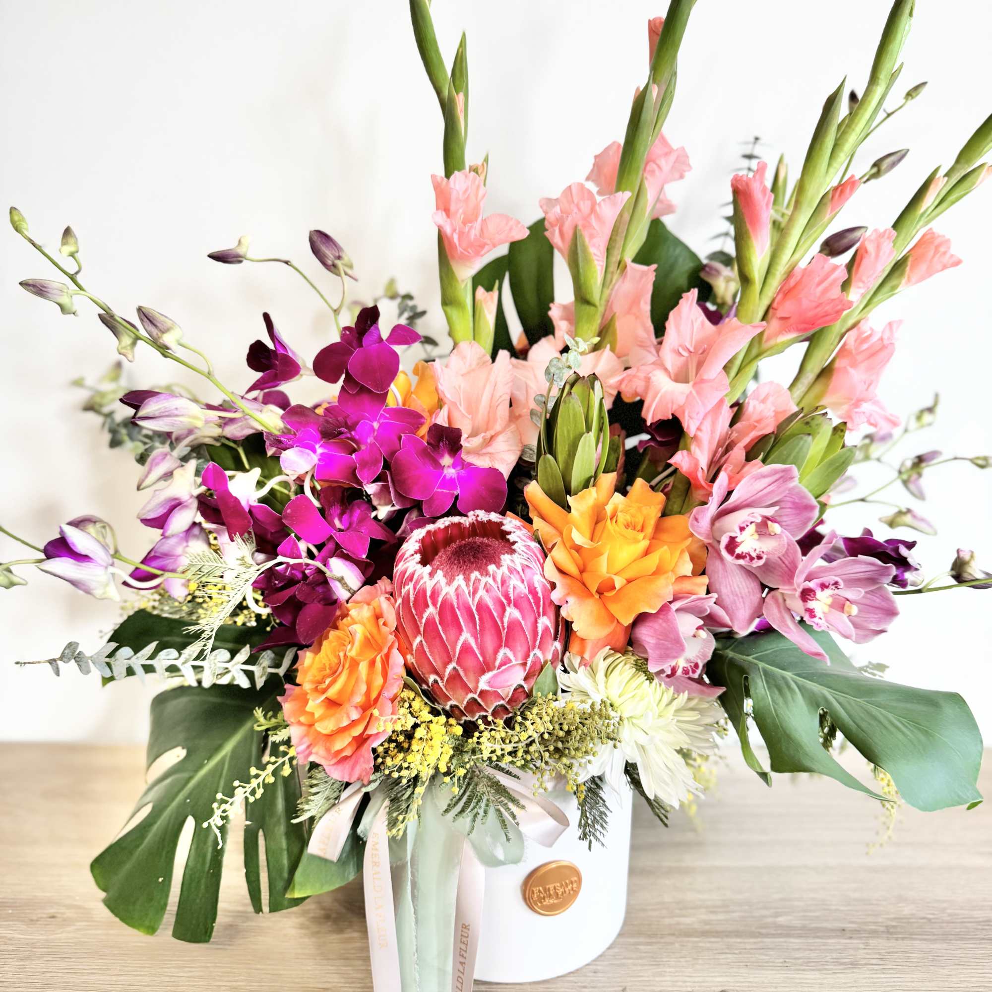Tropical bouquet with pink orchids and a protea in a white hatbox
