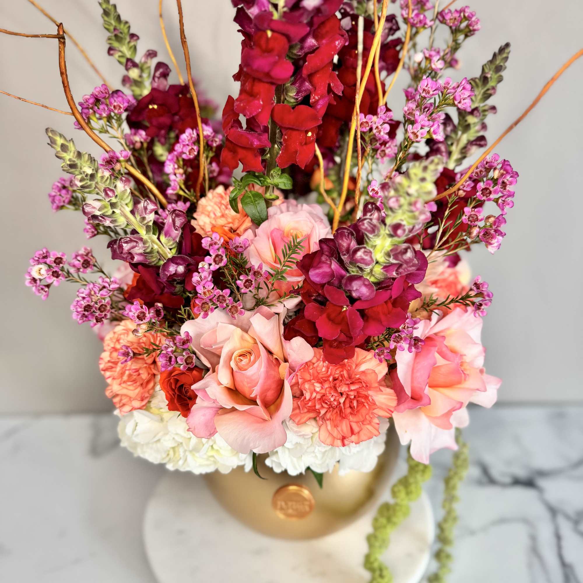 Tall floral arrangement with pink roses and magenta snapdragons in a gold vase