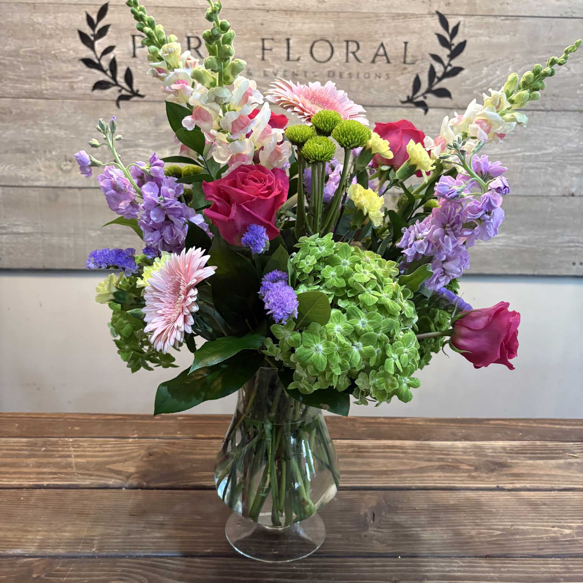 Bright pink roses and vivid gerbera daisies anchor this Secret Garden flower