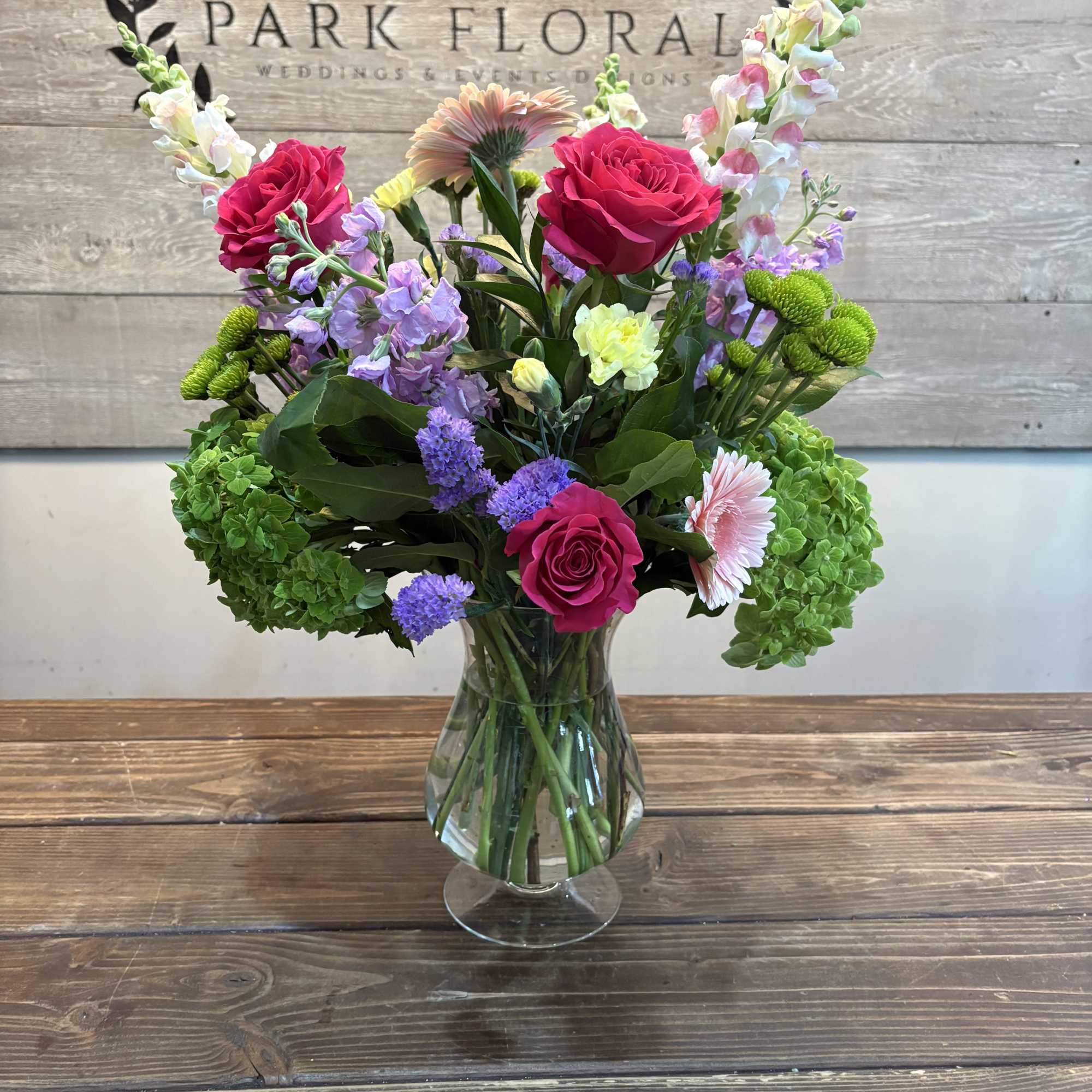 Bright pink roses and vivid gerbera daisies anchor this Secret Garden flower