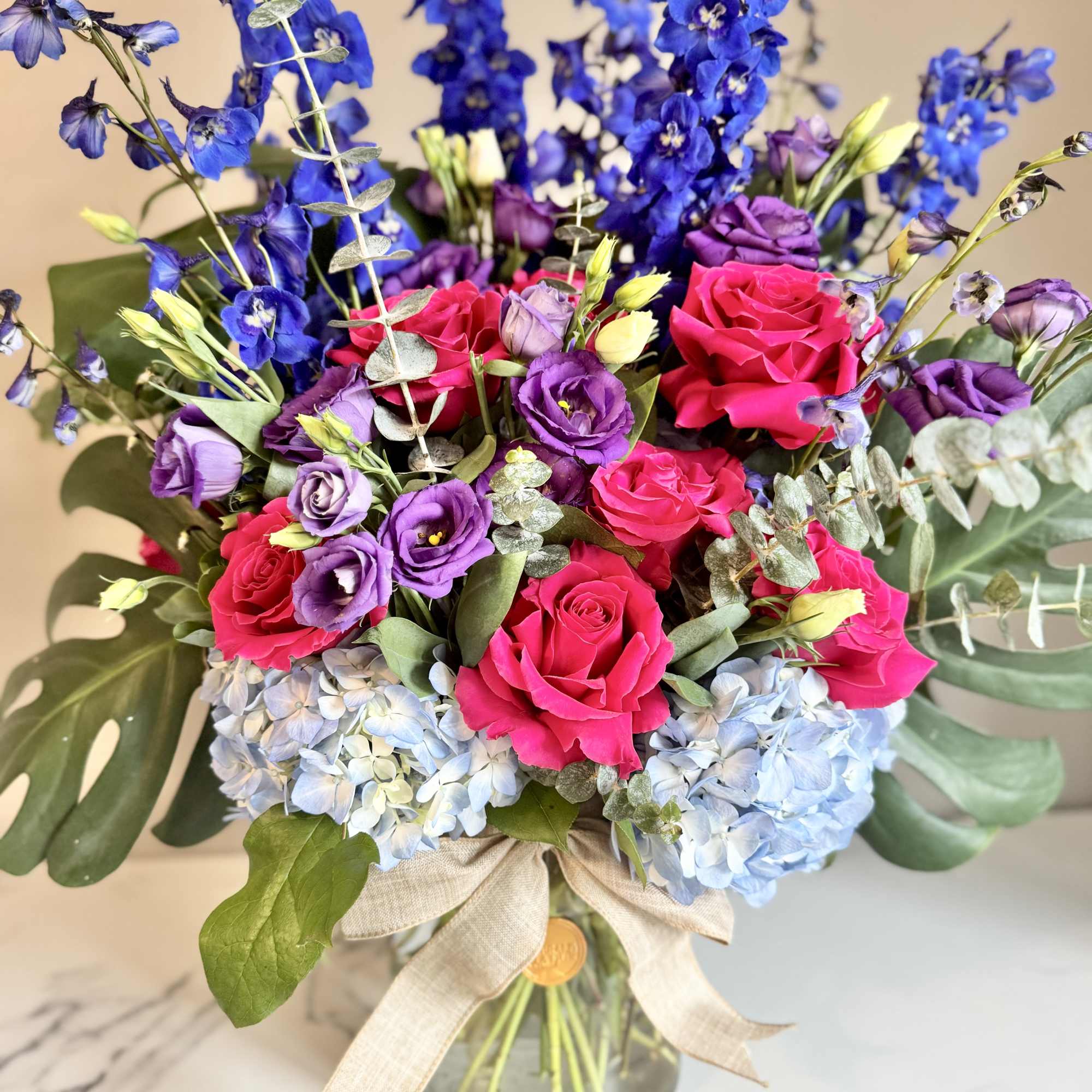 Bouquet of pink roses, purple blooms, and blue flowers in a glass vase