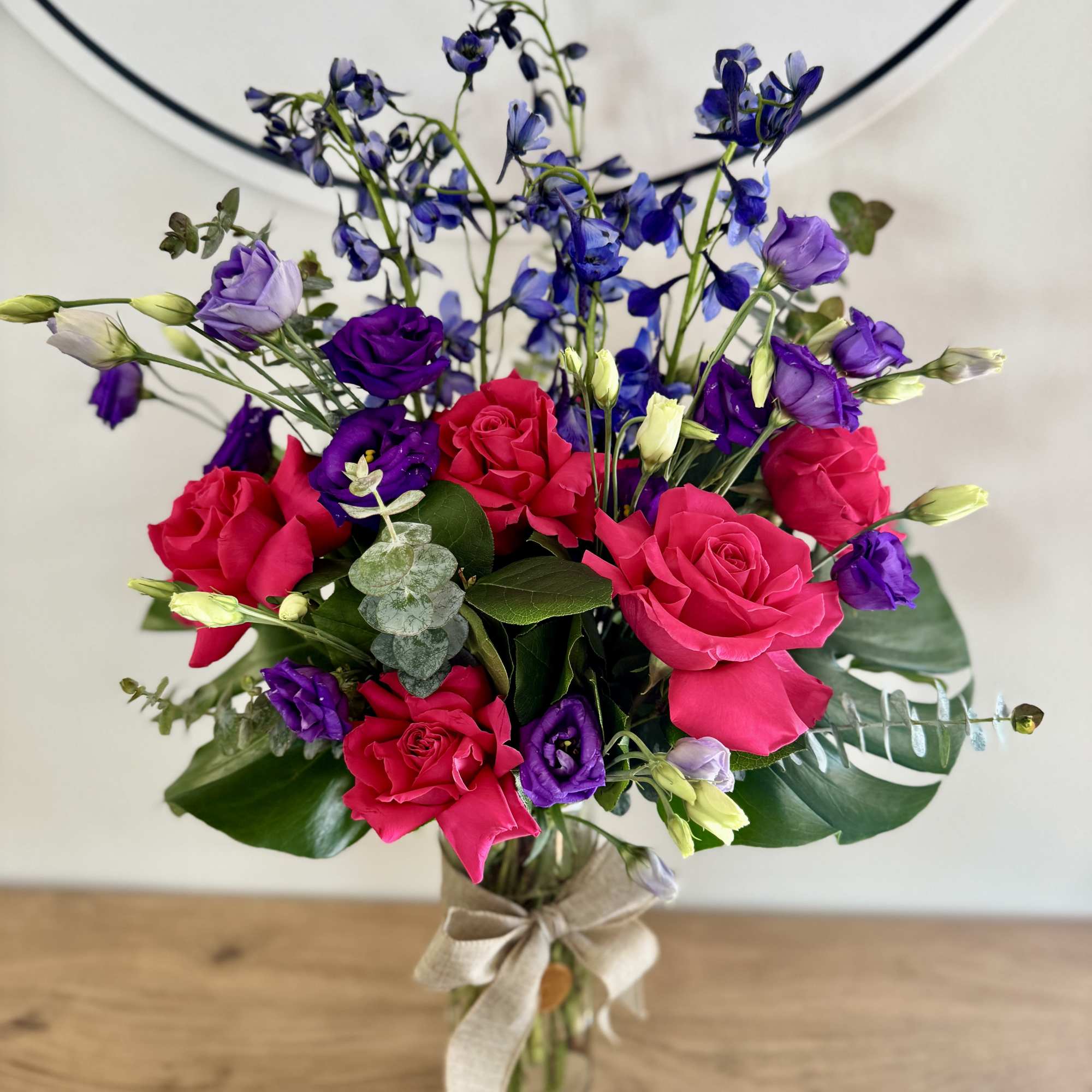 Featuring monstera leaves, delphinium, roses, and eucalyptus, this blue, green, and red