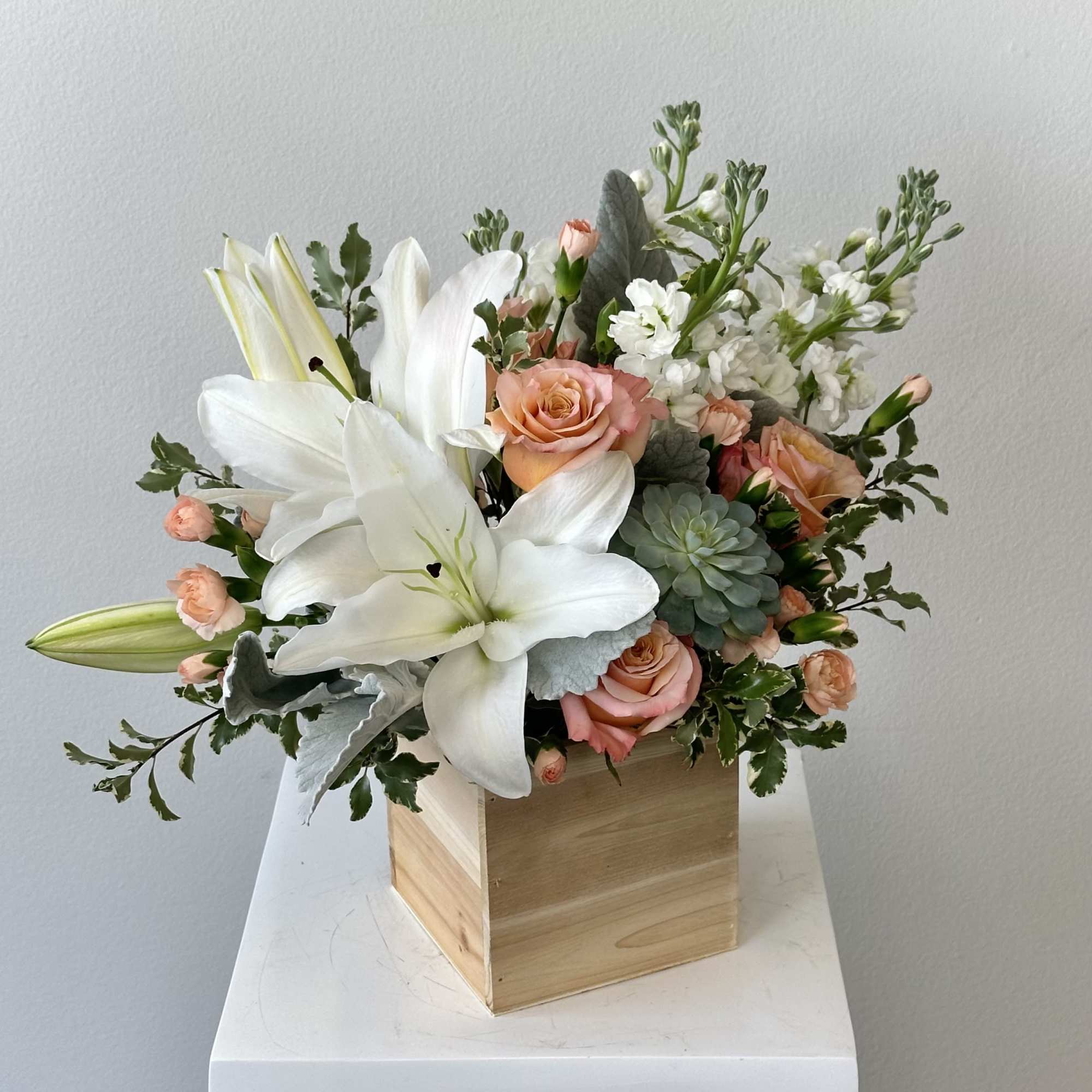 Wooden box arrangement with white lilies, peach roses, succulents, and white stock flowers