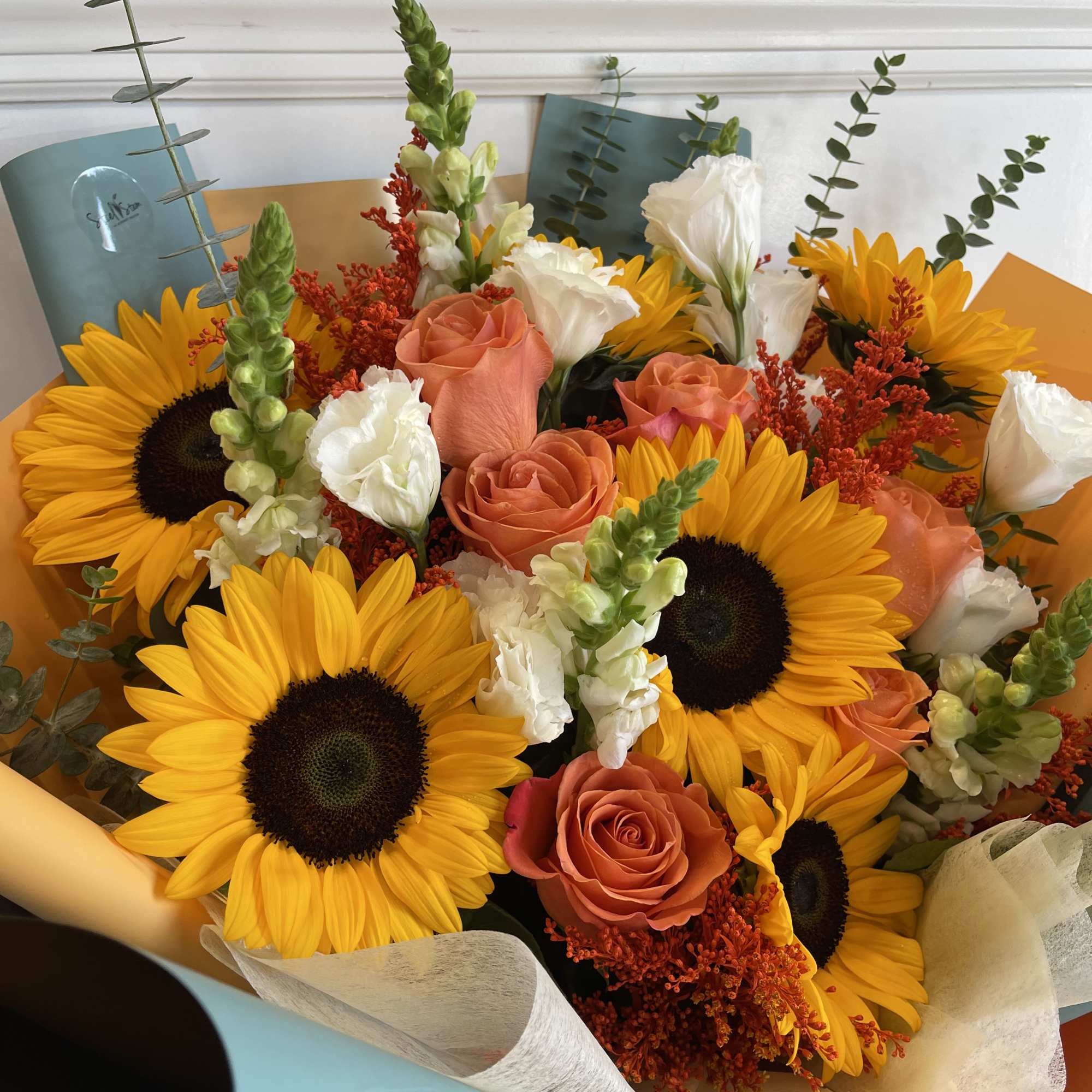 Bouquet of sunflowers, peach roses, and white blooms with orange wrapping