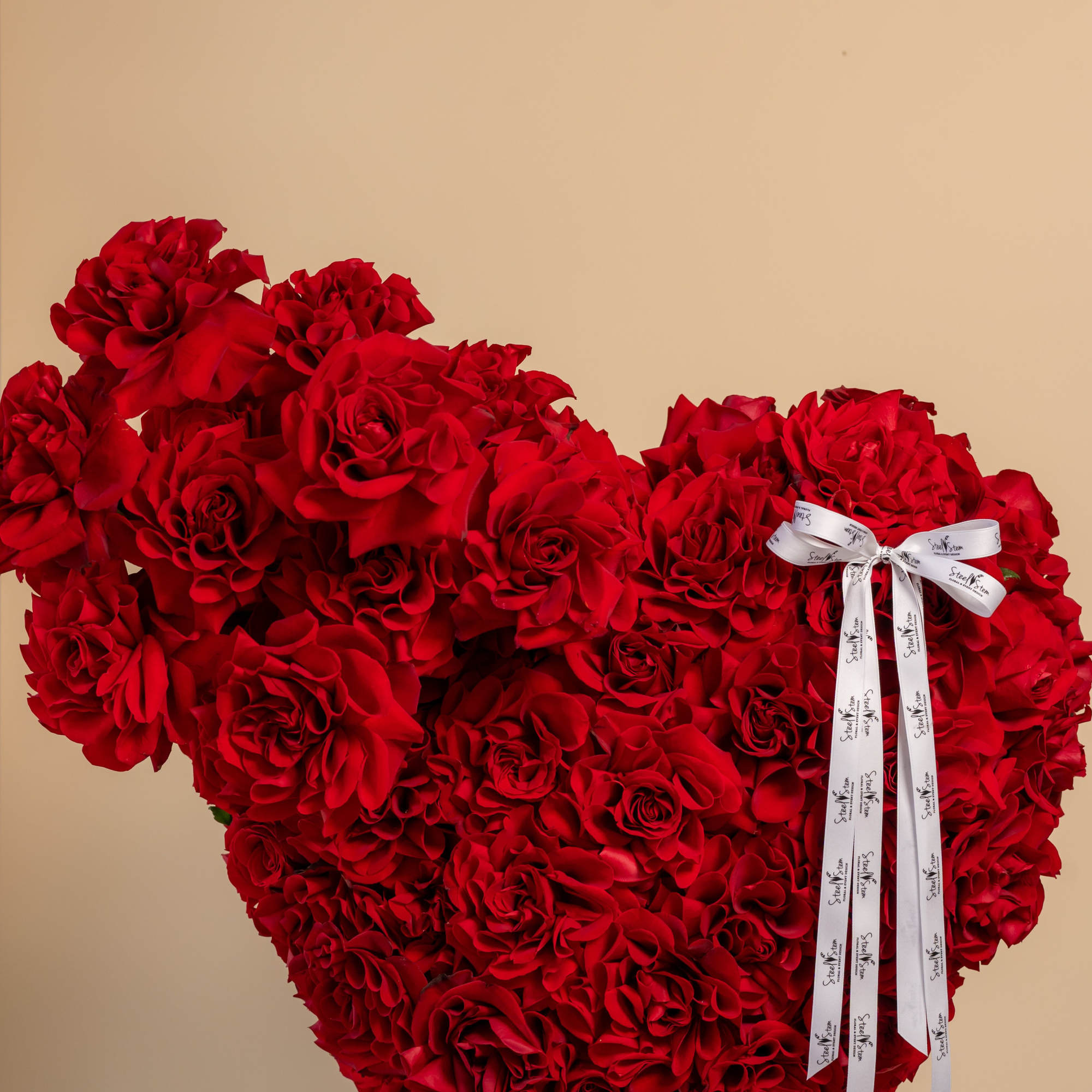 Heart-shaped arrangement of red roses with a white ribbon bow