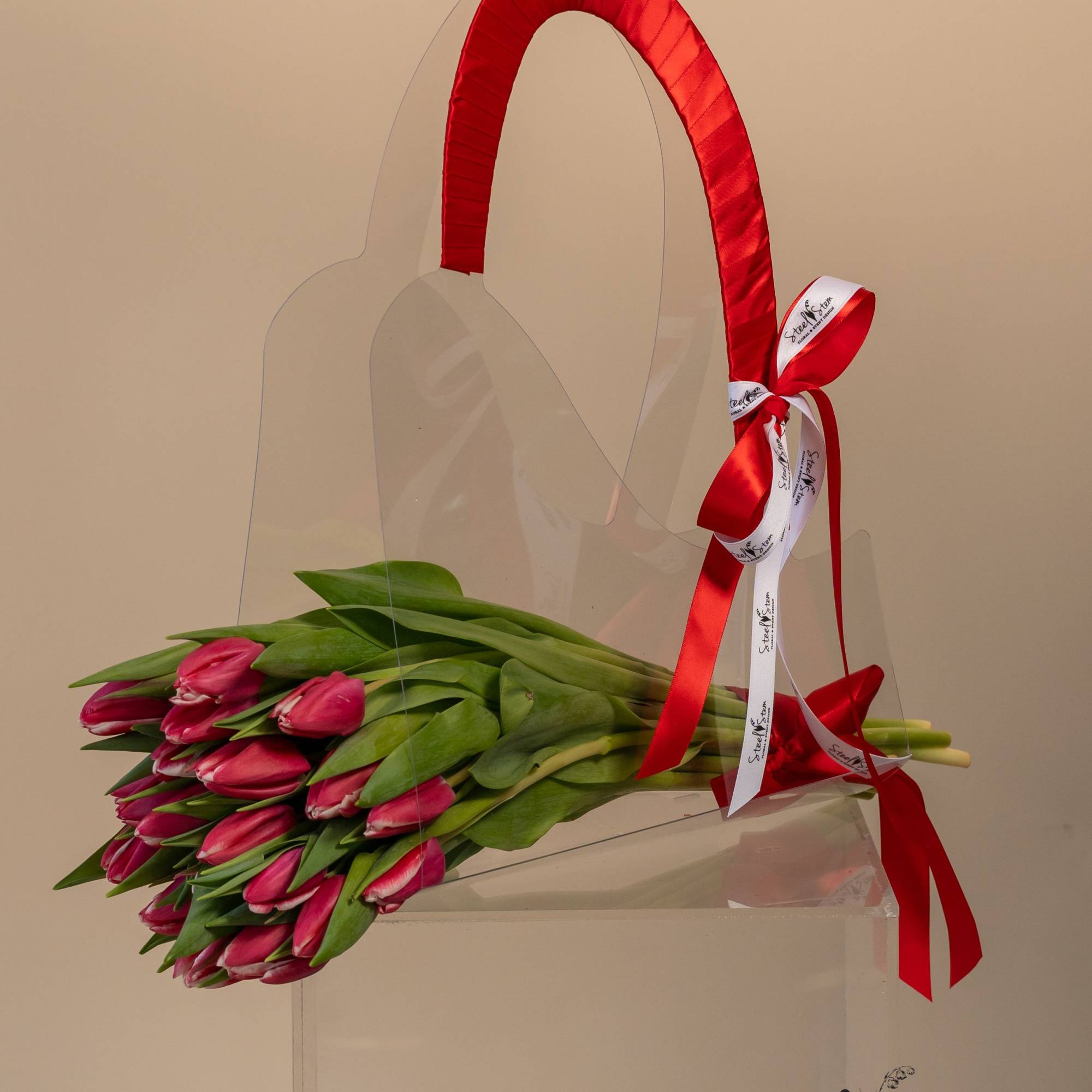 Bundle of pink tulips in a clear tote with a red ribbon handle