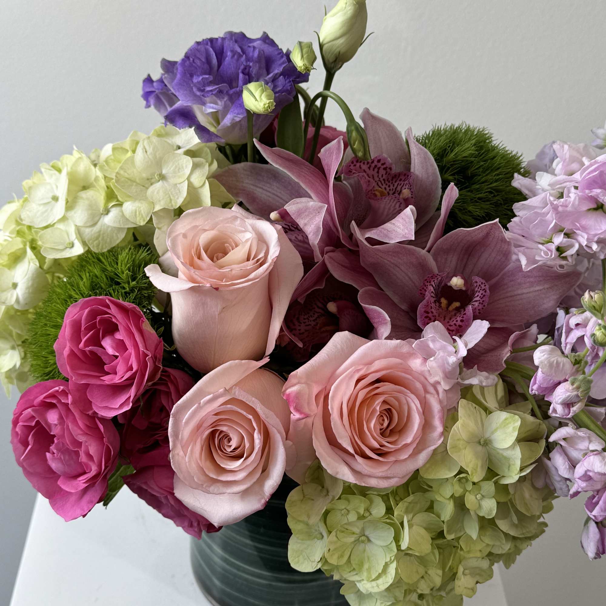 Bouquet of pink roses, purple orchids, and hydrangeas in a dark vase