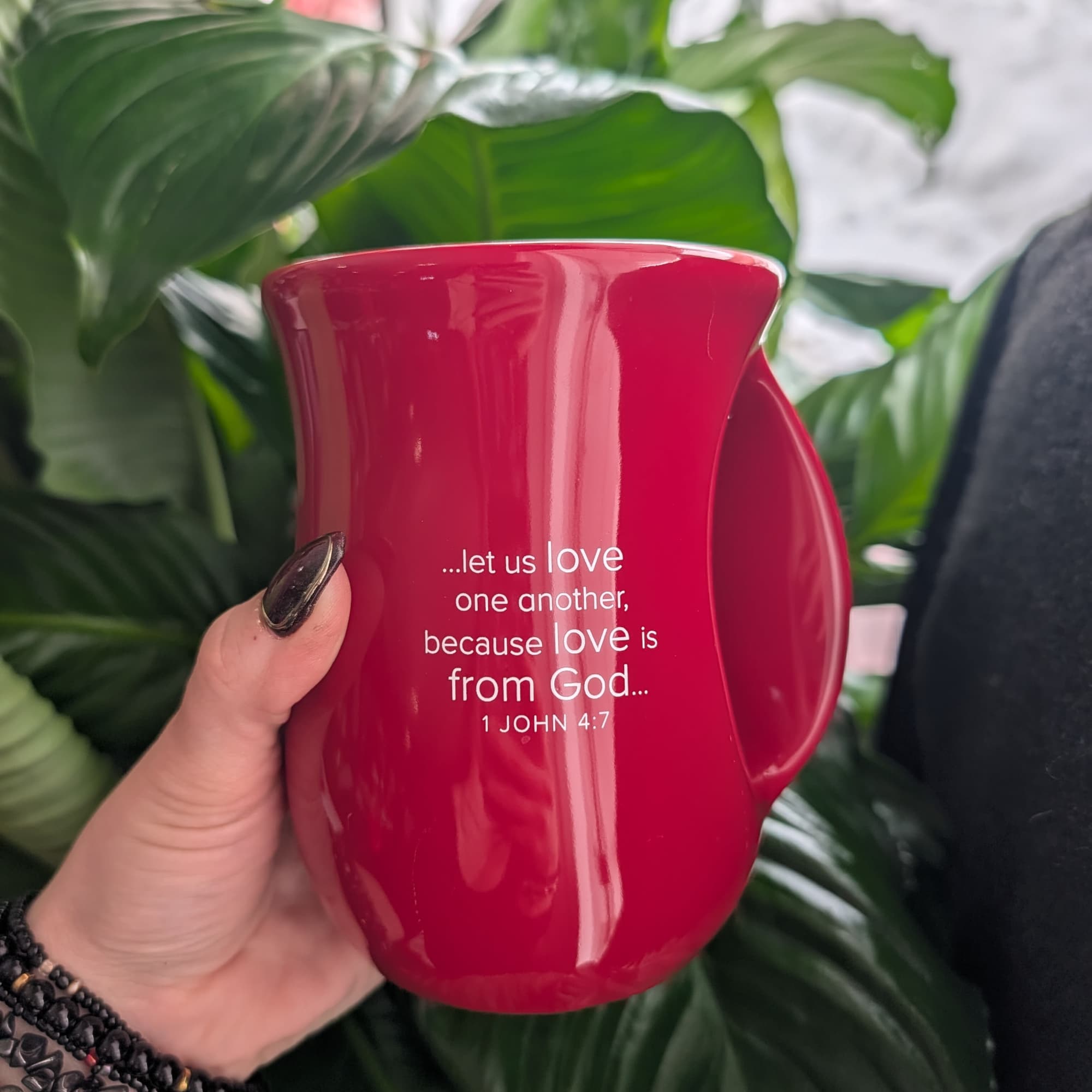 Red mug with a Bible verse held in front of green houseplants