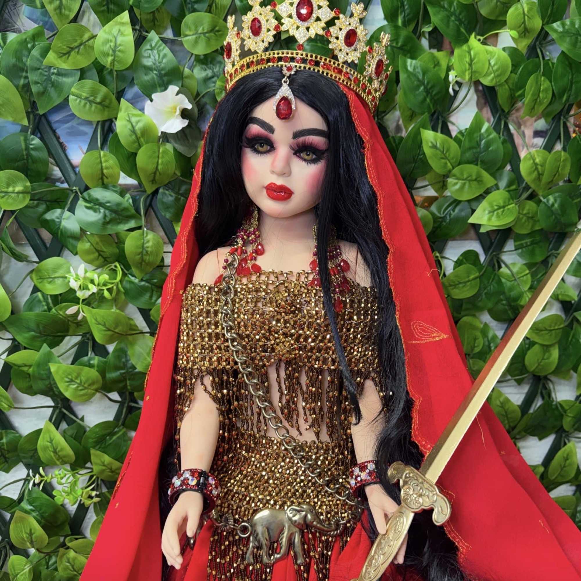 Decorative warrior doll in red-and-gold costume with jeweled crown, veil, and ornate