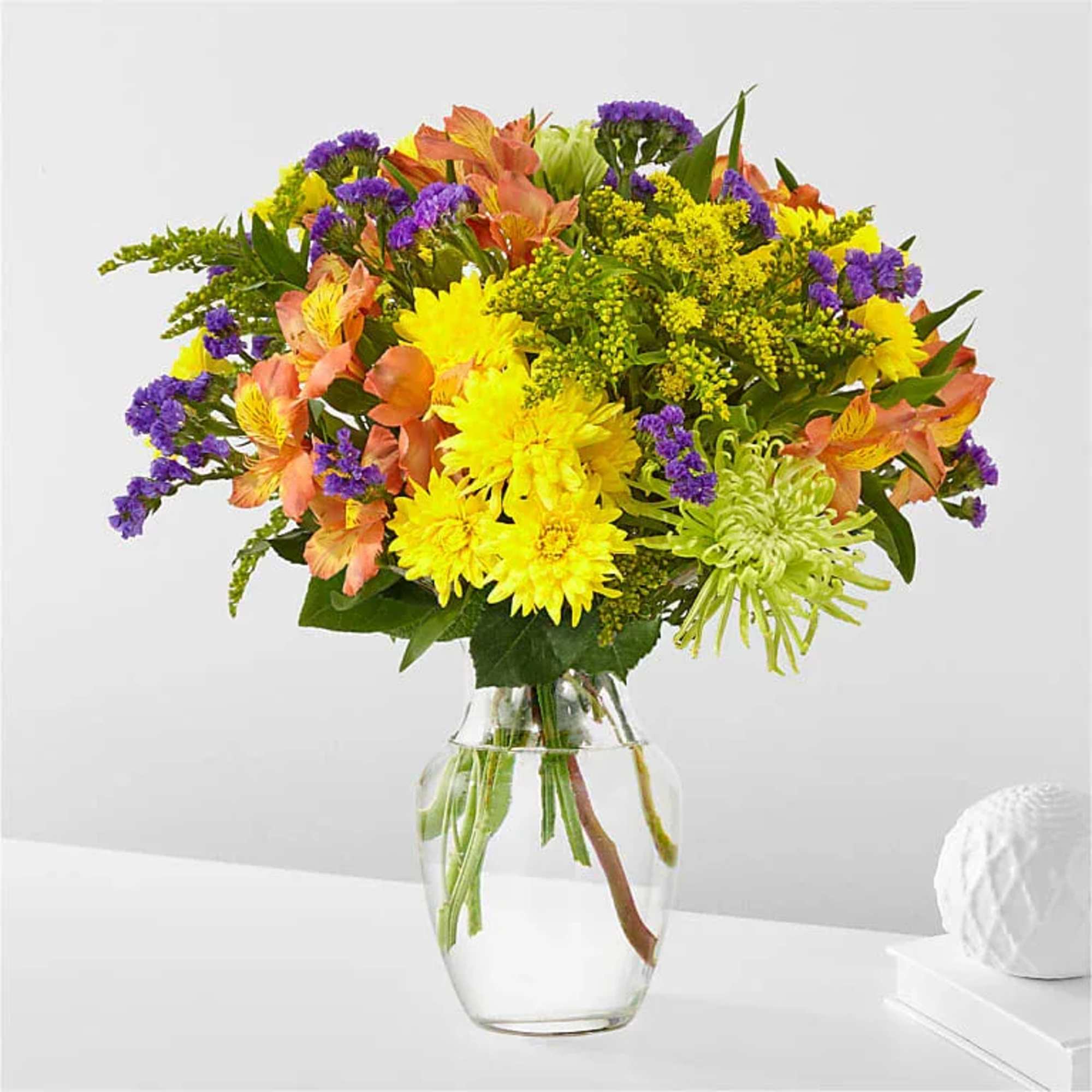 Mixed bouquet of yellow, purple, and peach flowers in a clear glass vase
