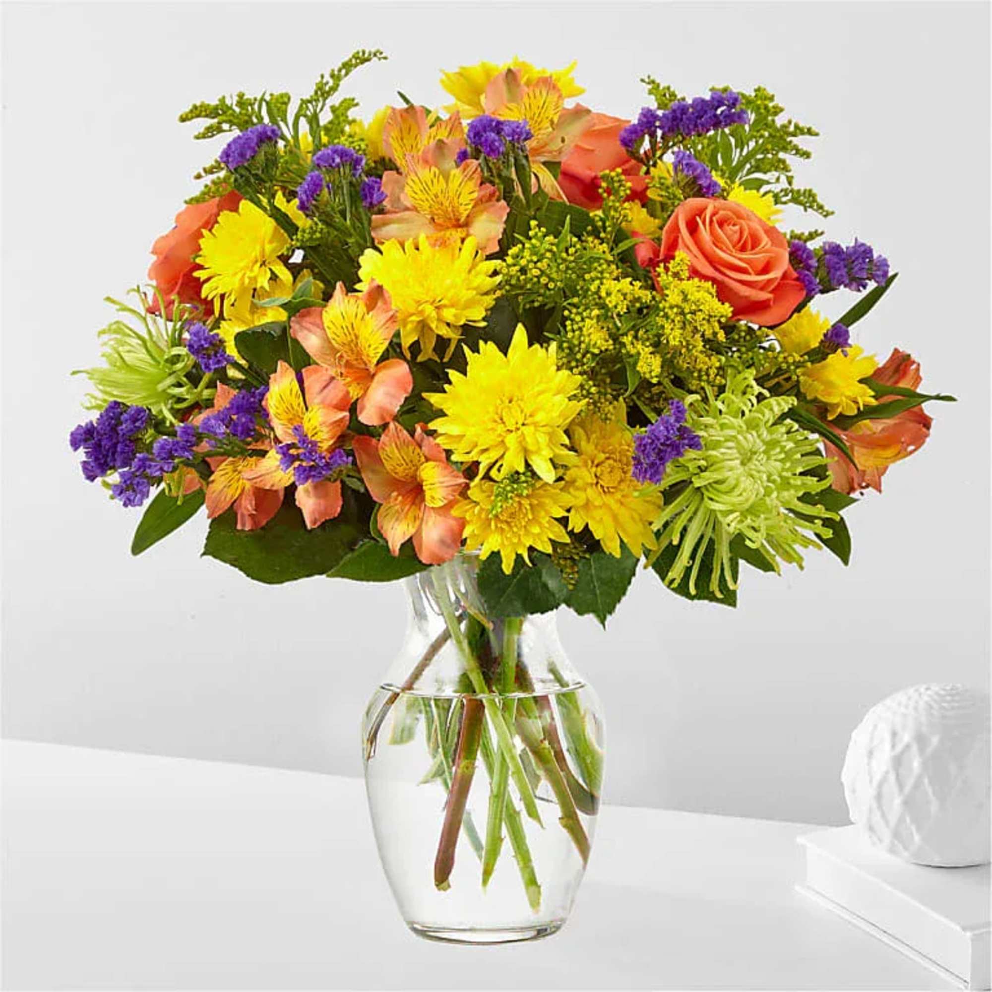 Mixed bouquet of yellow, orange, and purple flowers in a clear glass vase