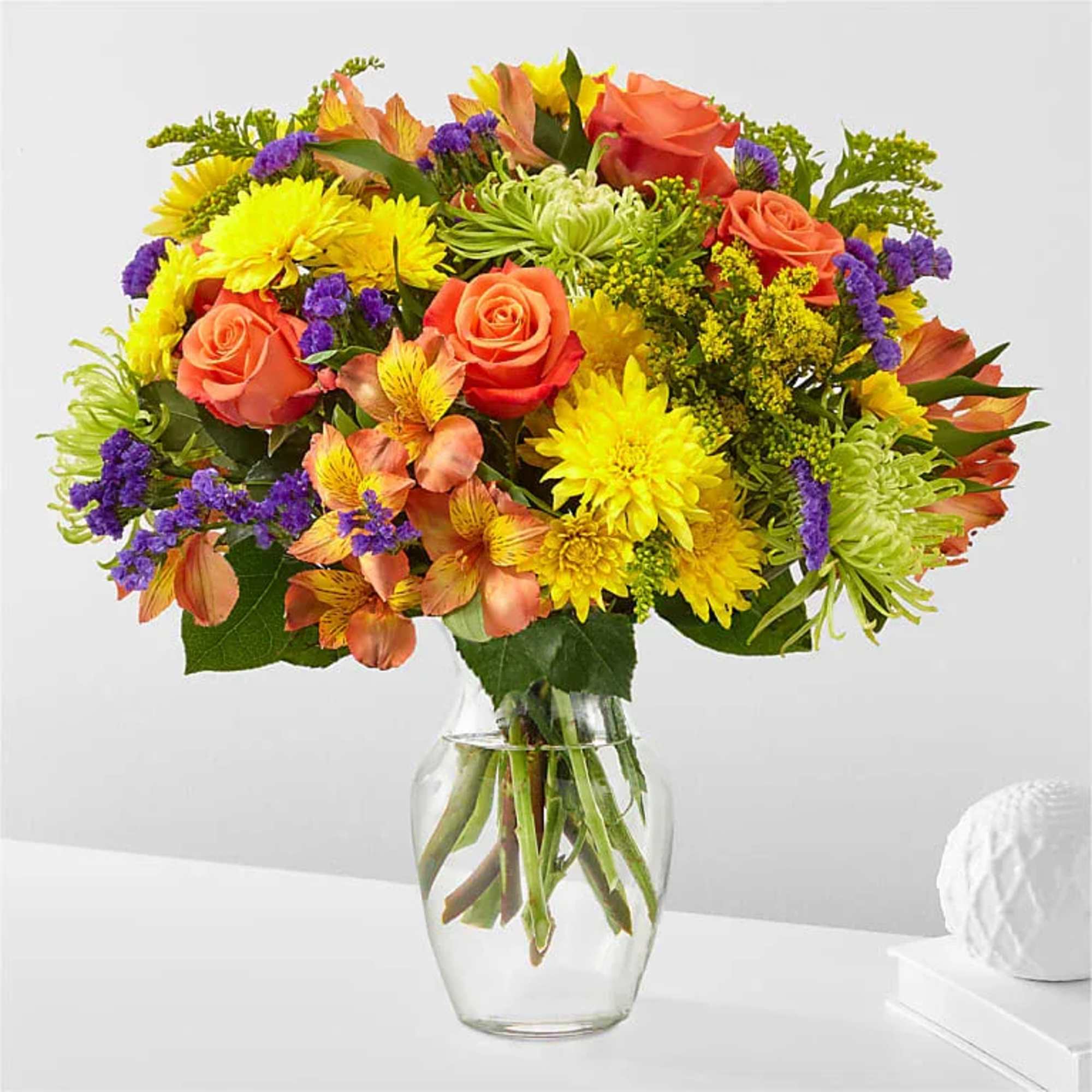 Colorful bouquet of roses, daisies, and mixed blooms in a clear glass vase