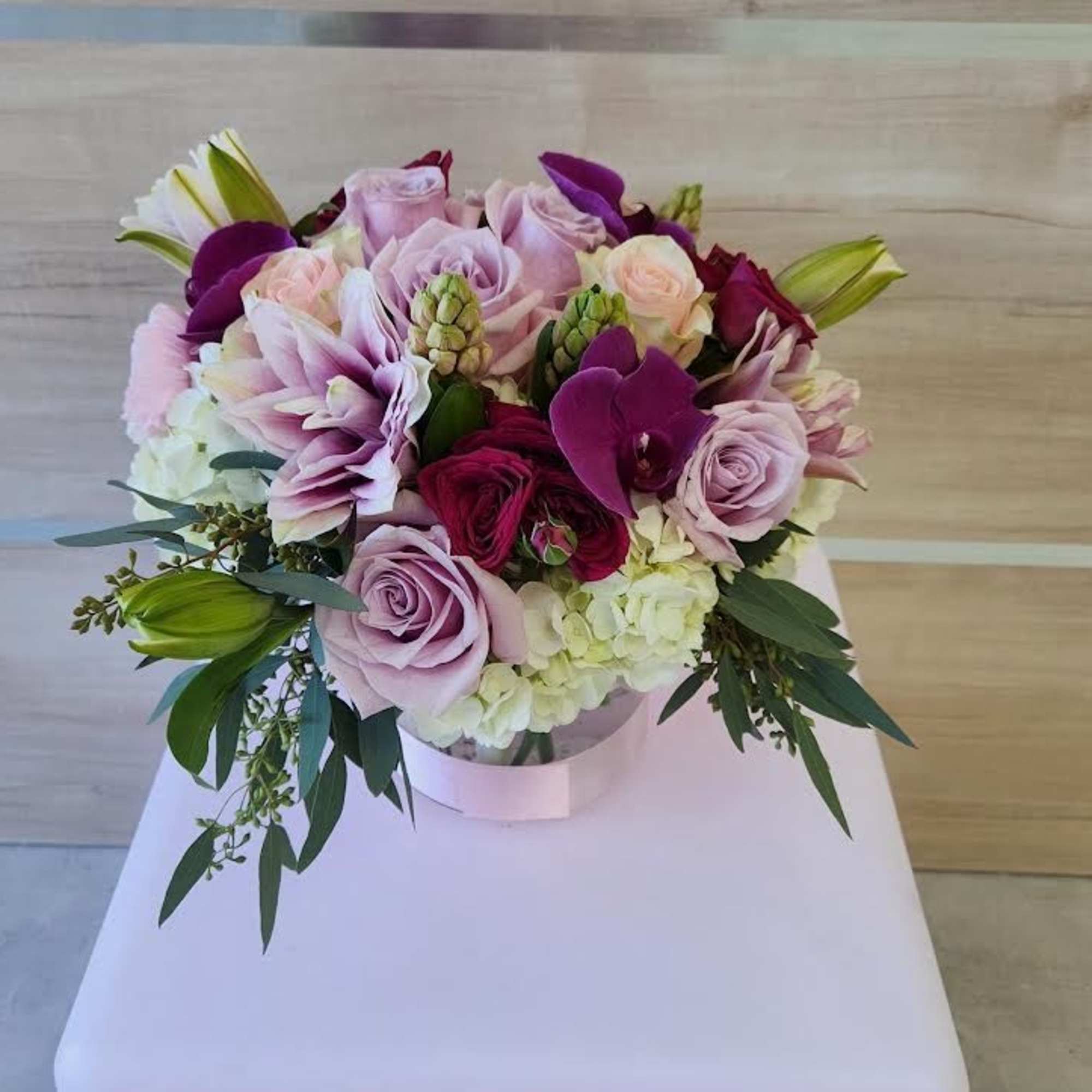 Round arrangement of pink roses, orchids, lilies and white hydrangeas in a low clear vase