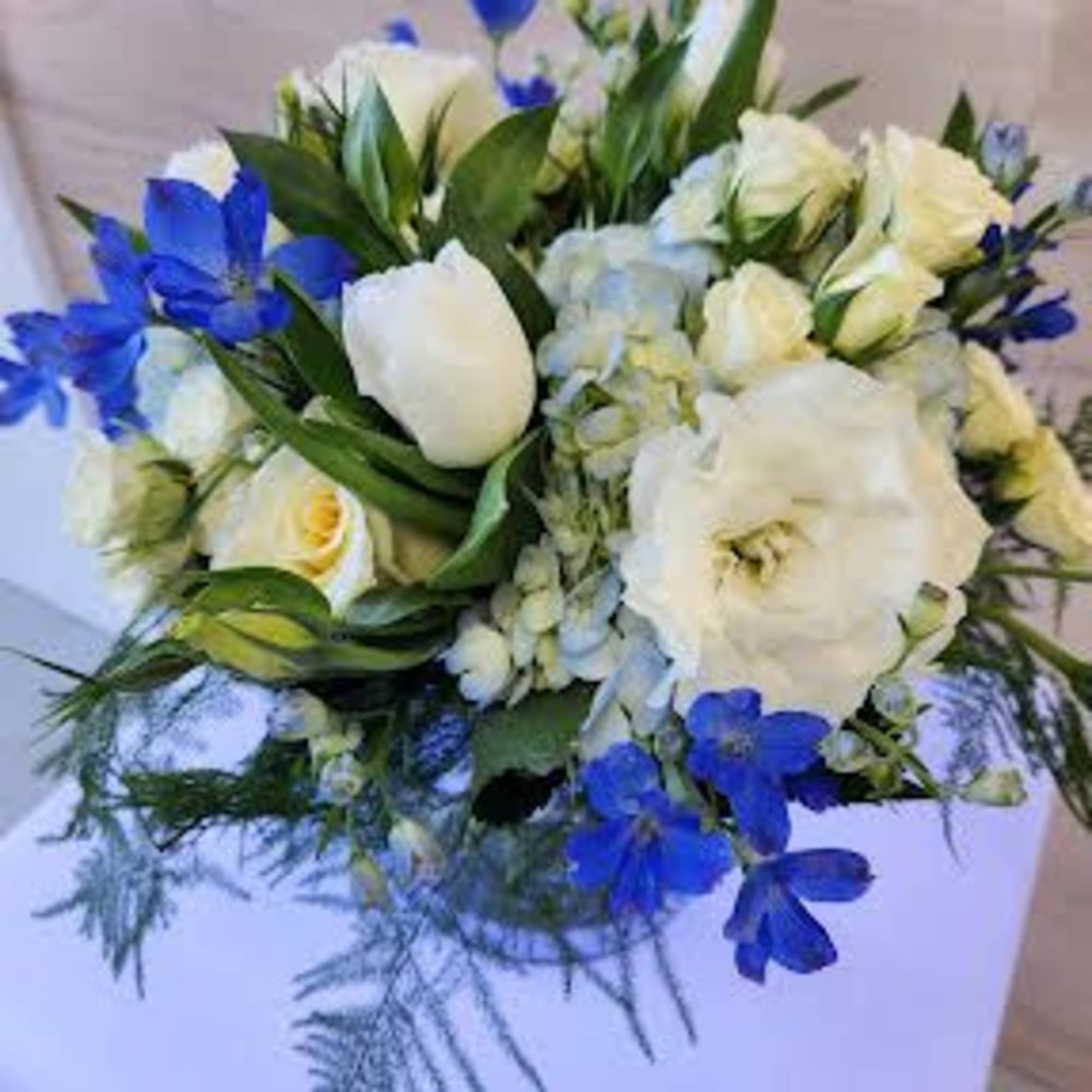 Low round arrangement of white roses, hydrangeas, and blue flowers on a white-covered table