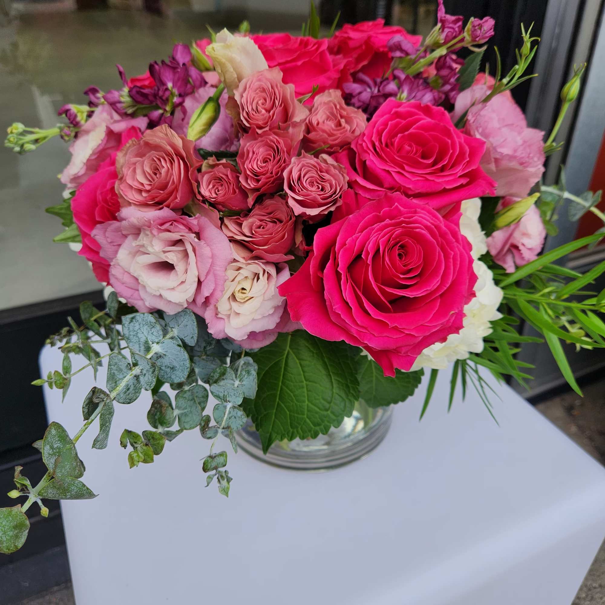 Low arrangement of hot pink roses and blush flowers in a glass vase on a white table