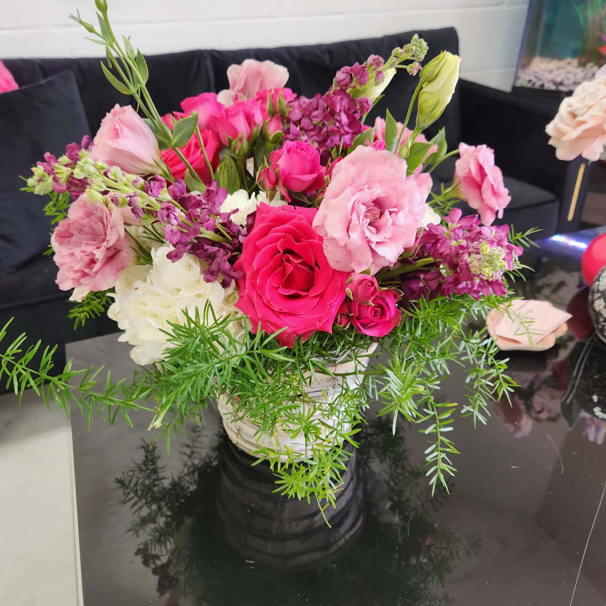 Mixed pink and white flower arrangement with trailing greenery in a white pot on a black table