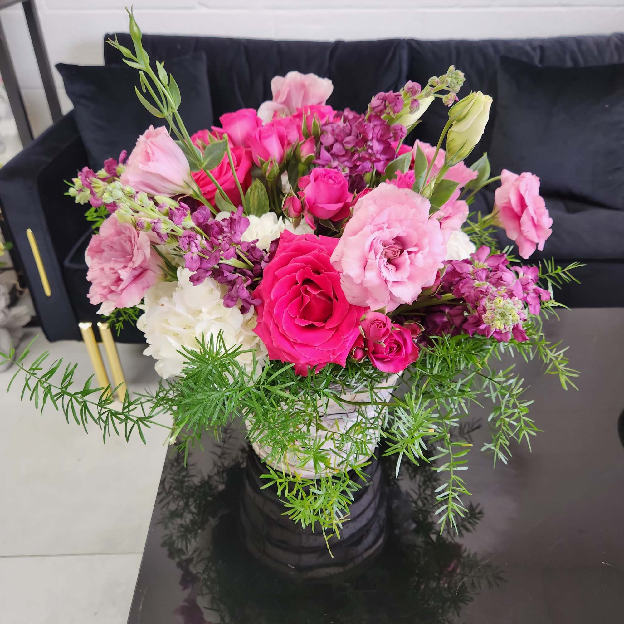 Bright pink and purple mixed flower arrangement in a white pot on a black table