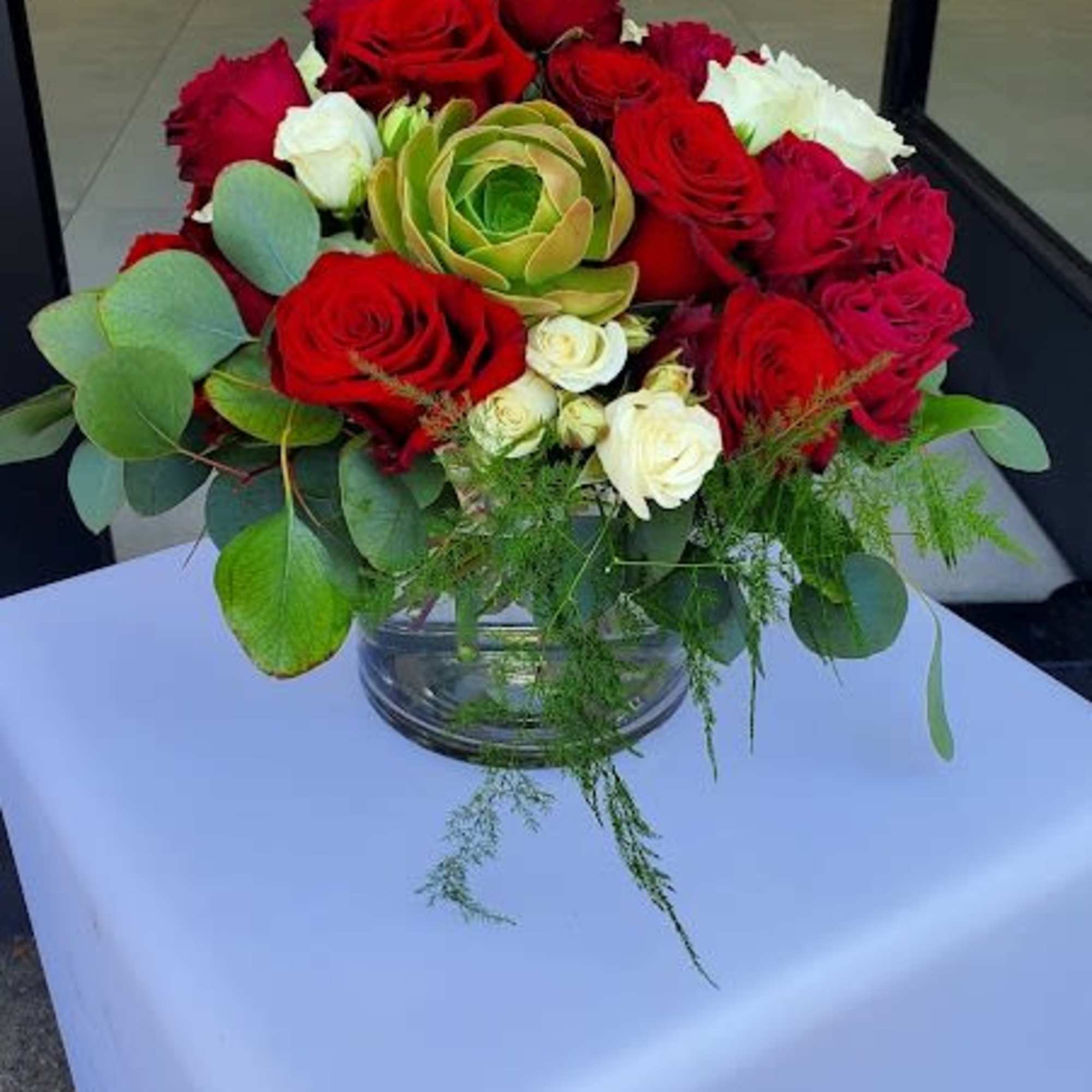 Low round arrangement of red and white roses with a green succulent in a clear glass bowl vase