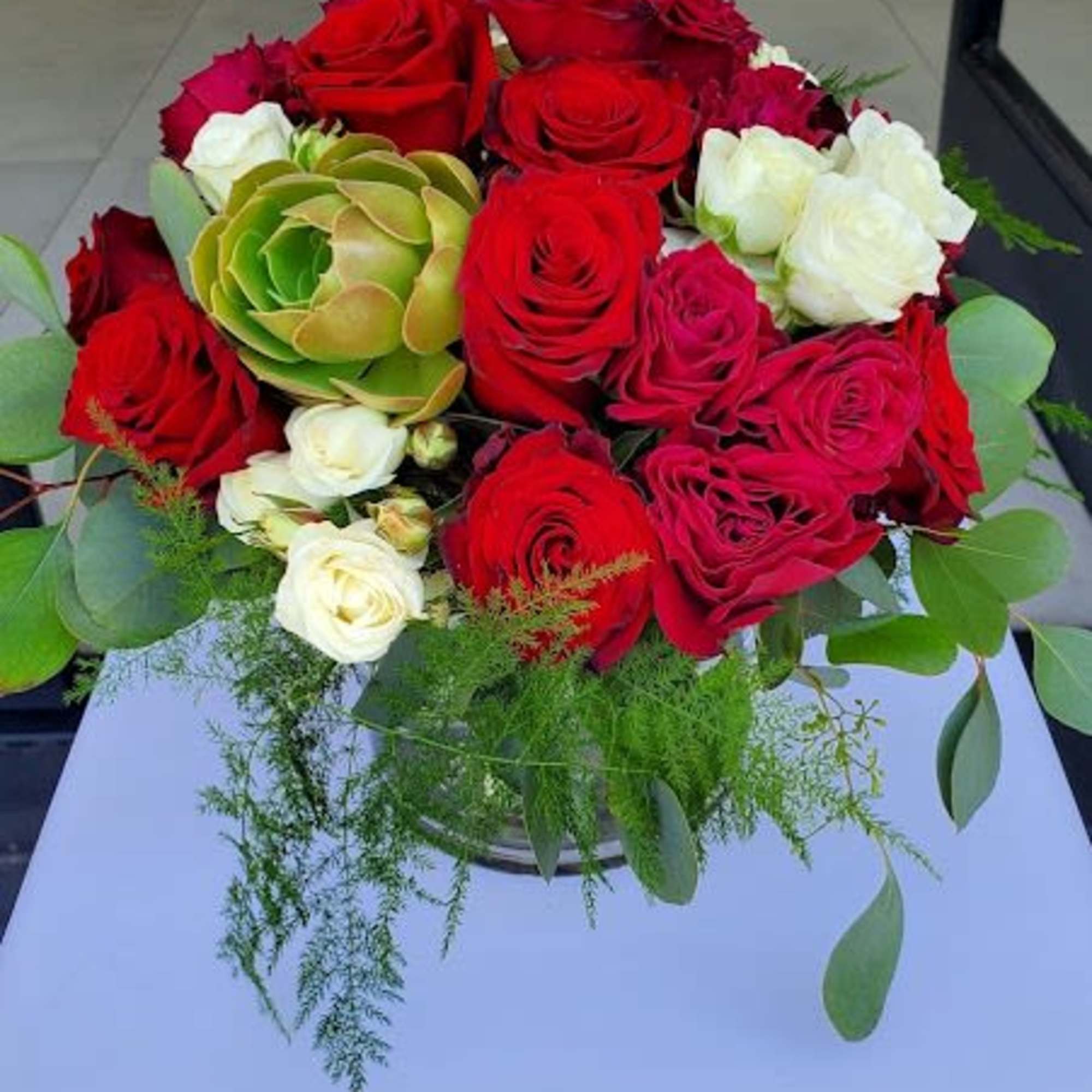Low round arrangement of red and white roses with a central green succulent in a clear glass vase