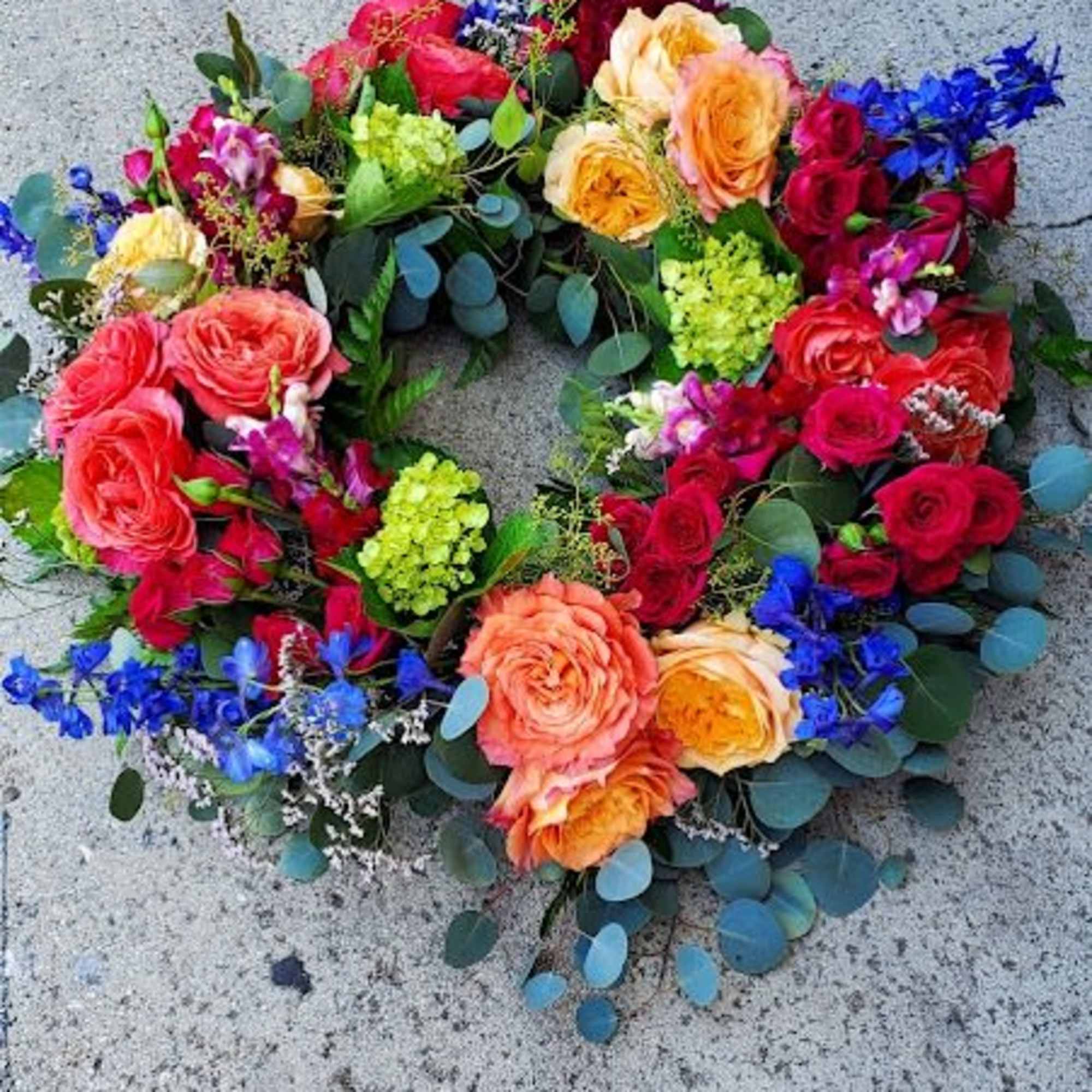Colorful circular wreath with red, orange, green, and blue flowers on a concrete surface