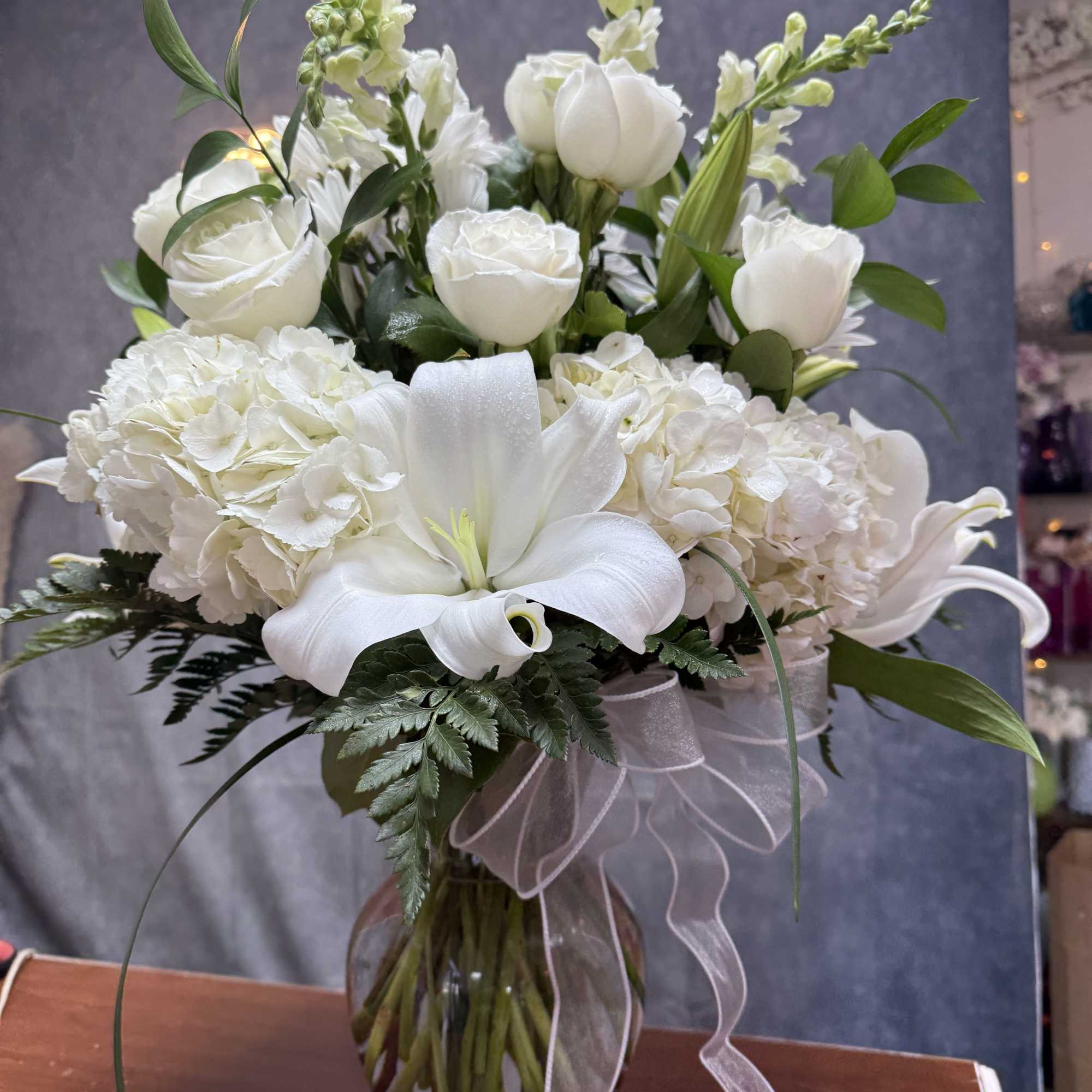 White lilies, roses, and hydrangeas in a glass vase with a sheer ribbon