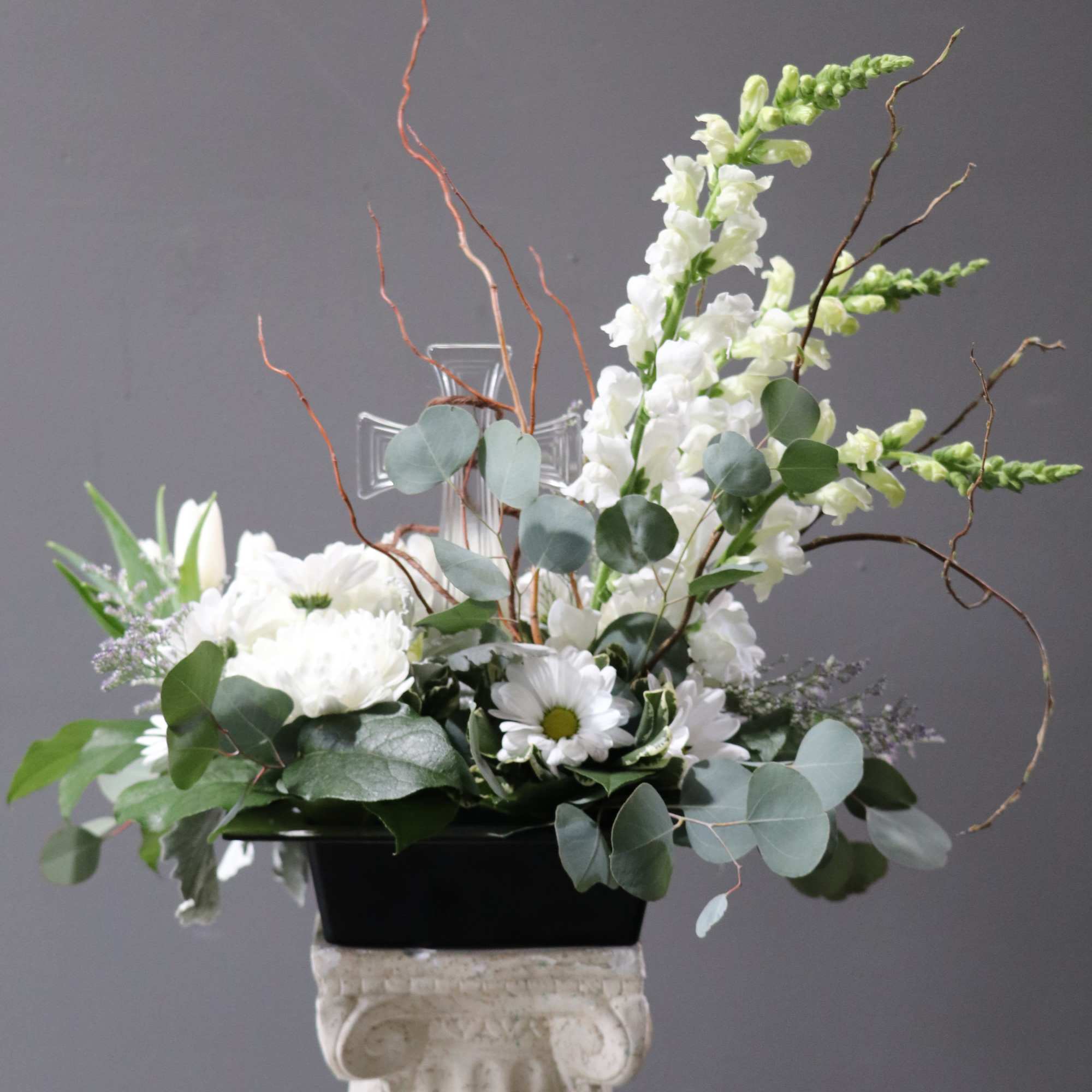 White floral arrangement in a black container with eucalyptus and curly branches