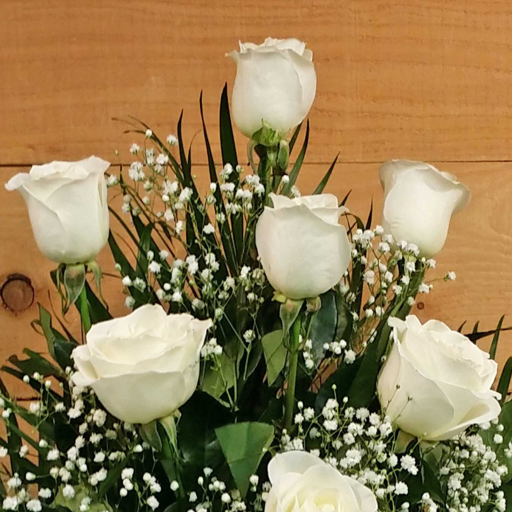 White roses arranged with baby's breath against a wood background