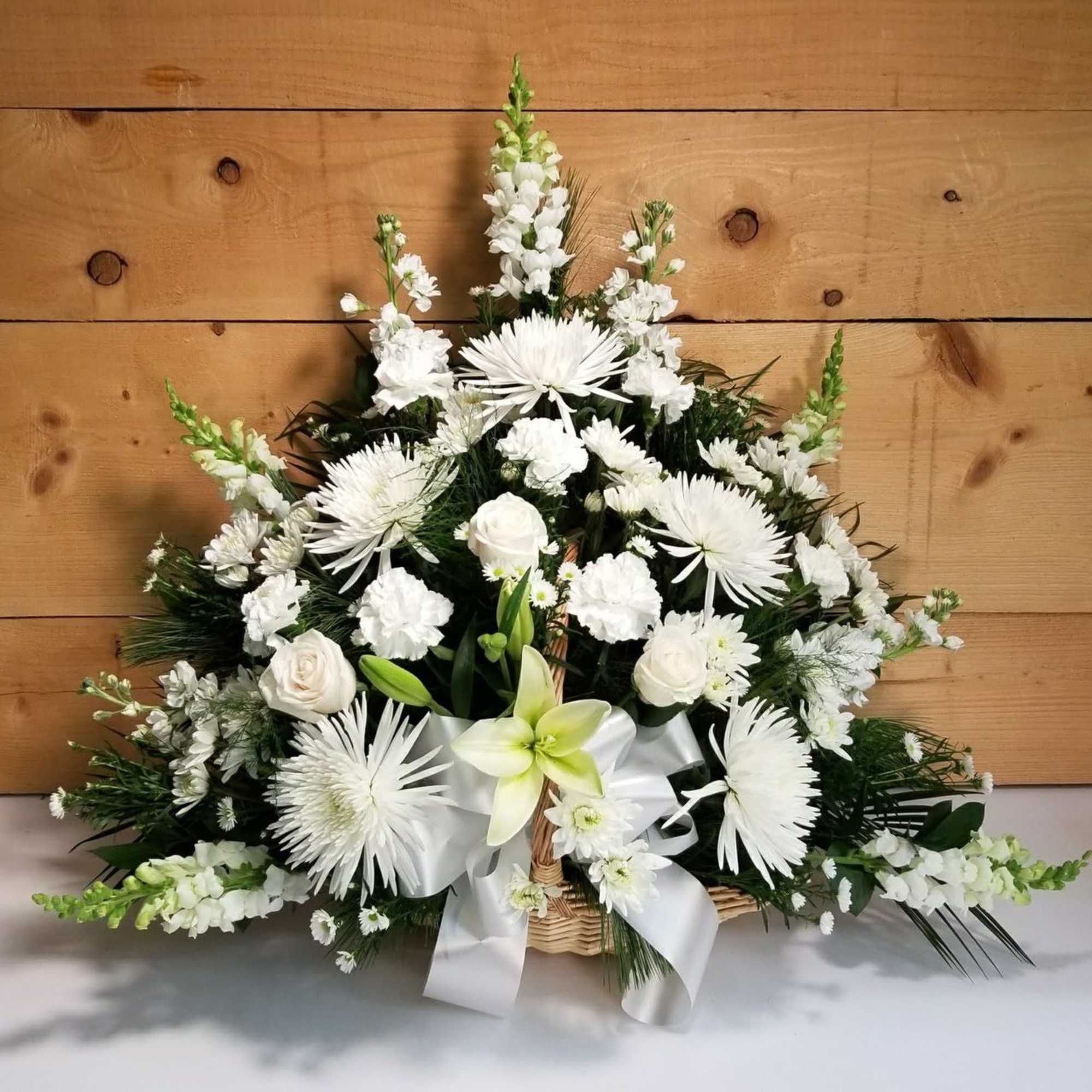 White floral arrangement in a wicker basket with a white ribbon
