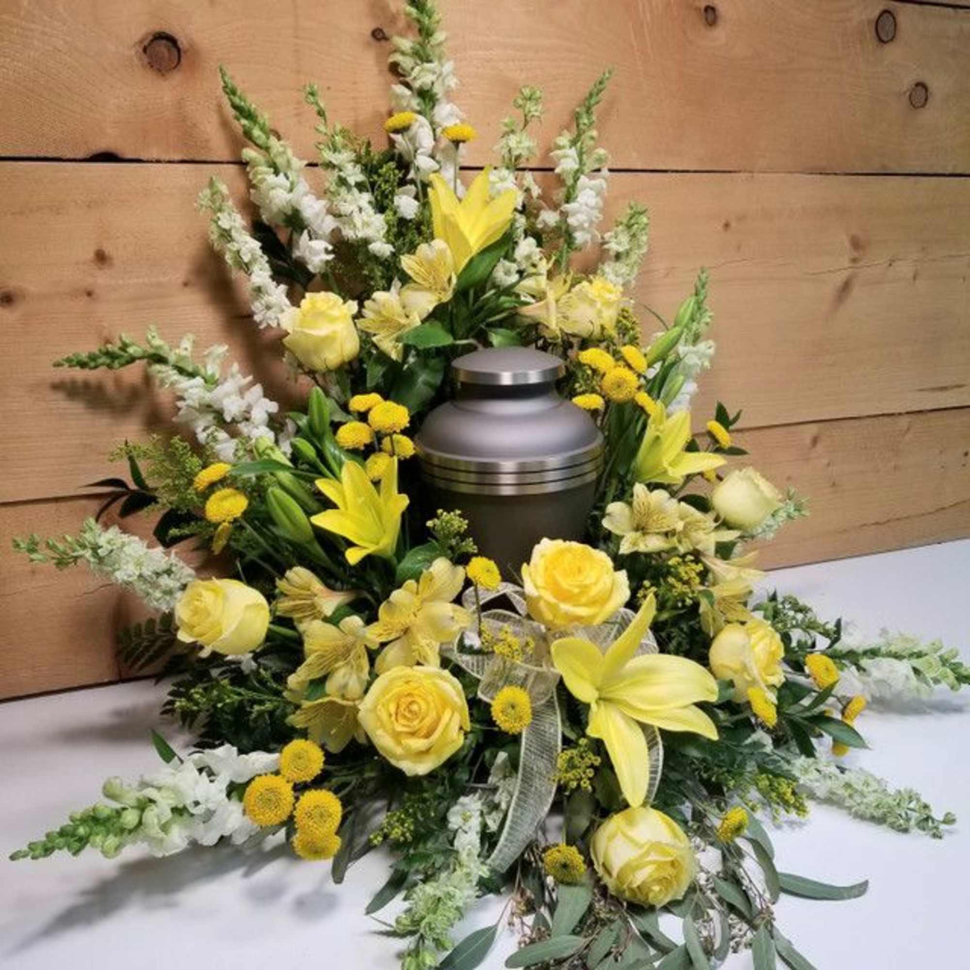 Yellow and white funeral floral arrangement around a metal urn
