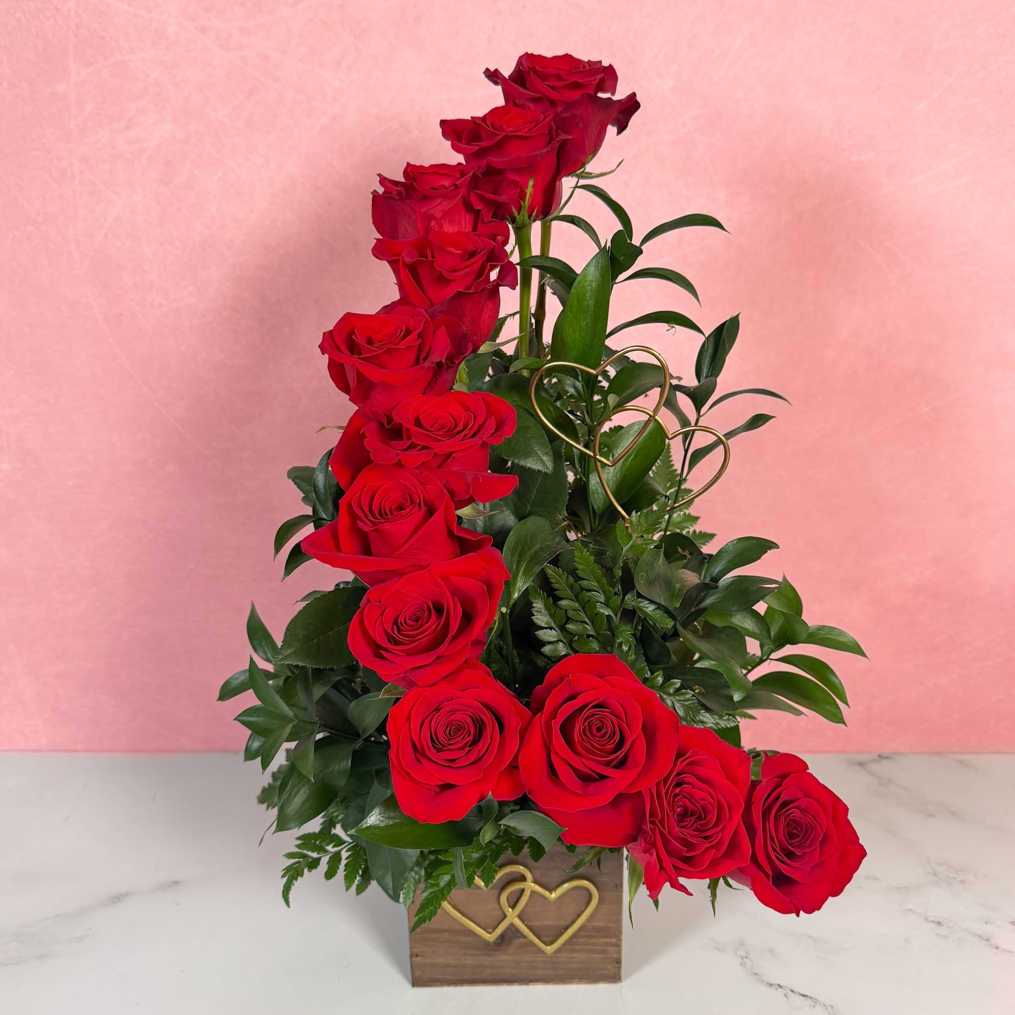 Tall arrangement of red roses in a wooden box with gold heart accents