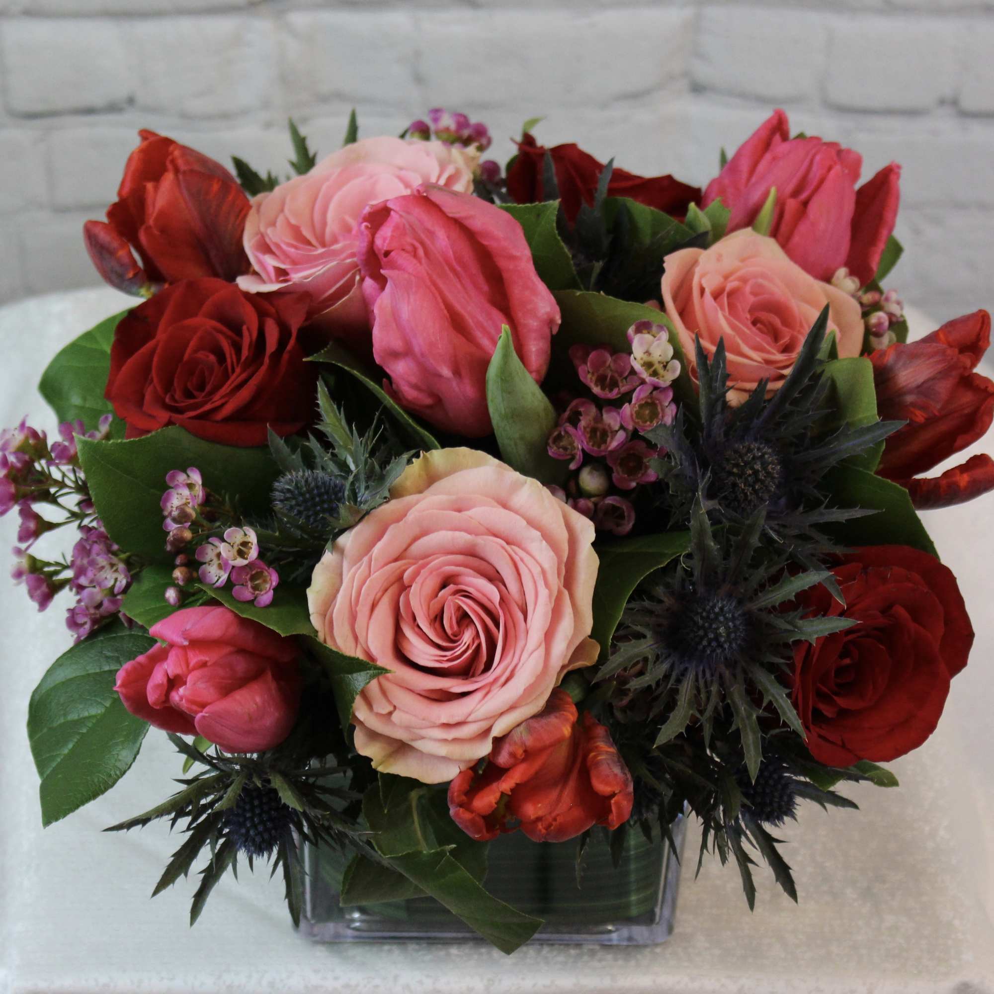 Bouquet of pink and red roses with dark thistle in a clear square vase