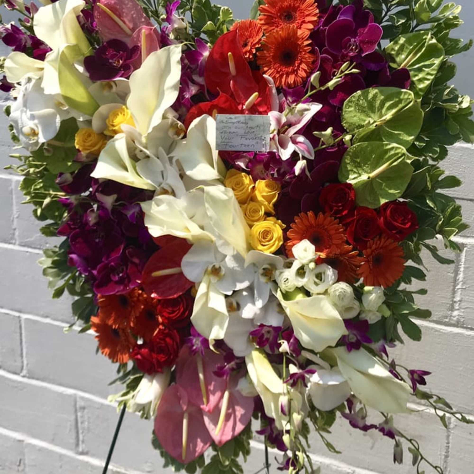 Heart-shaped floral spray with white calla lilies, orchids, and red gerberas