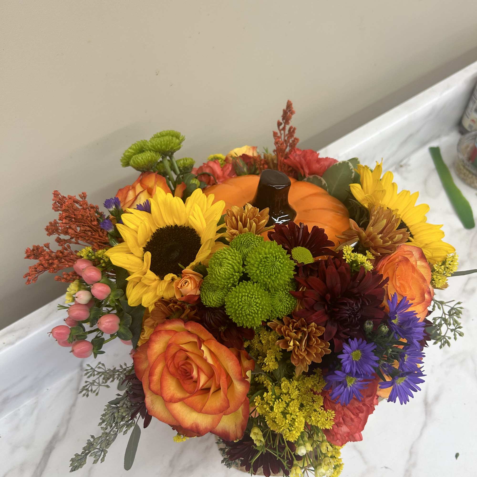 Colorful bouquet with sunflowers, roses, and chrysanthemums around a pumpkin