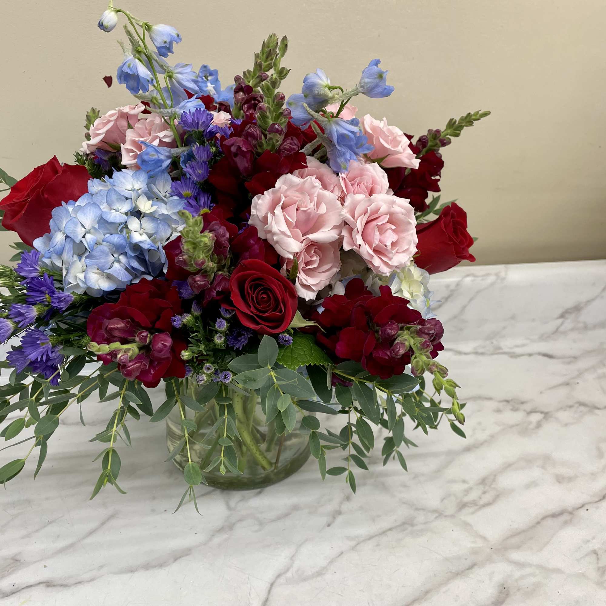 Mixed bouquet of red, pink, and blue flowers in a glass vase