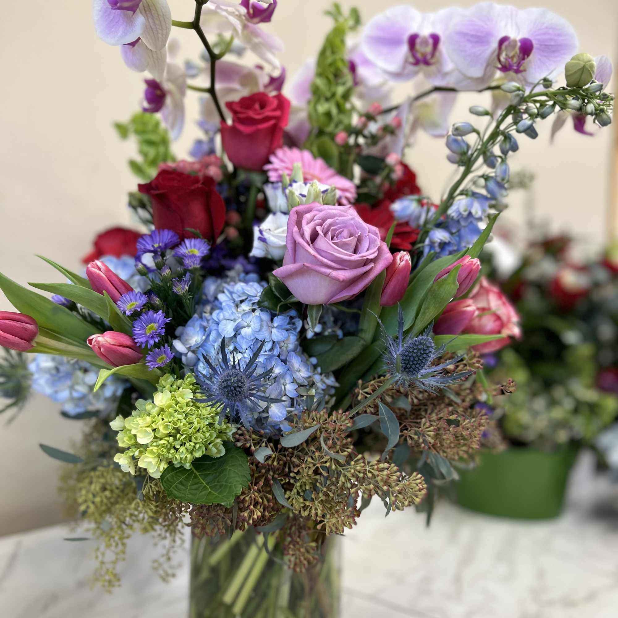 Mixed bouquet with orchids, roses, hydrangeas, and tulips in a glass vase