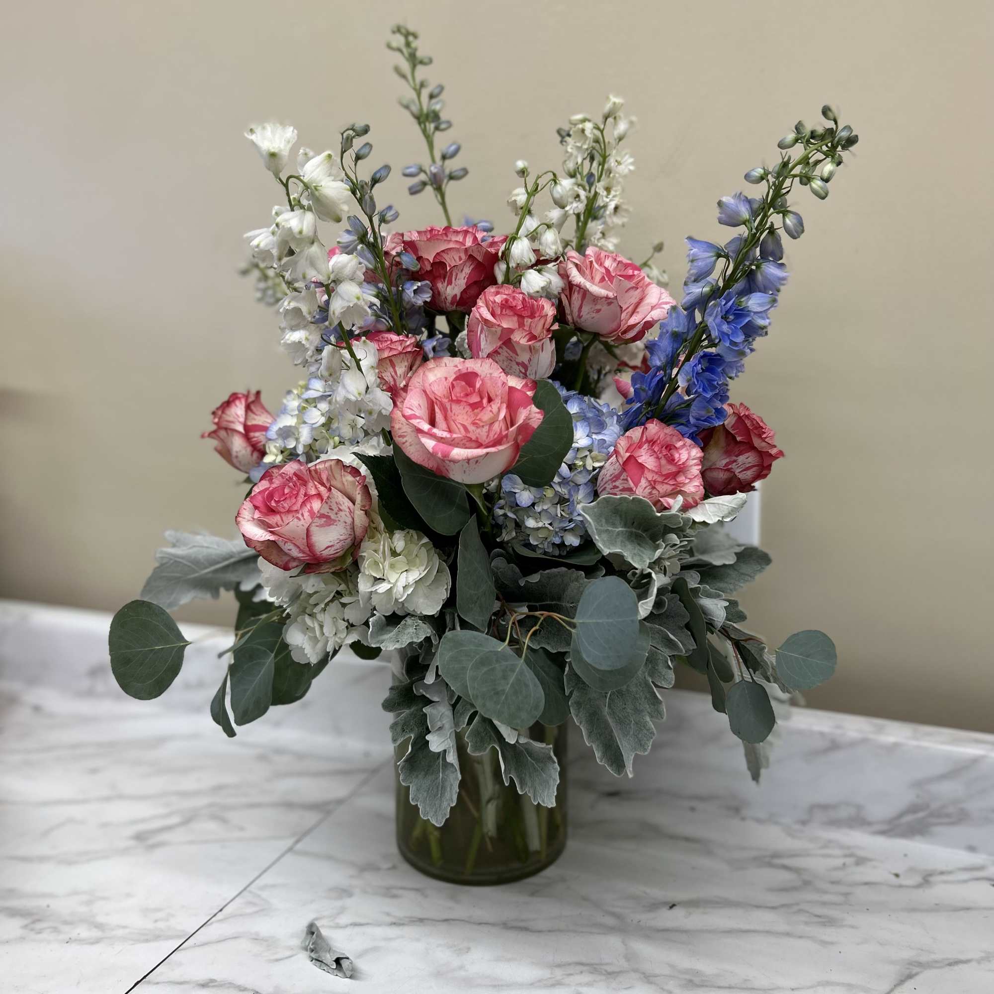 Pink and white roses with blue delphinium in a glass vase