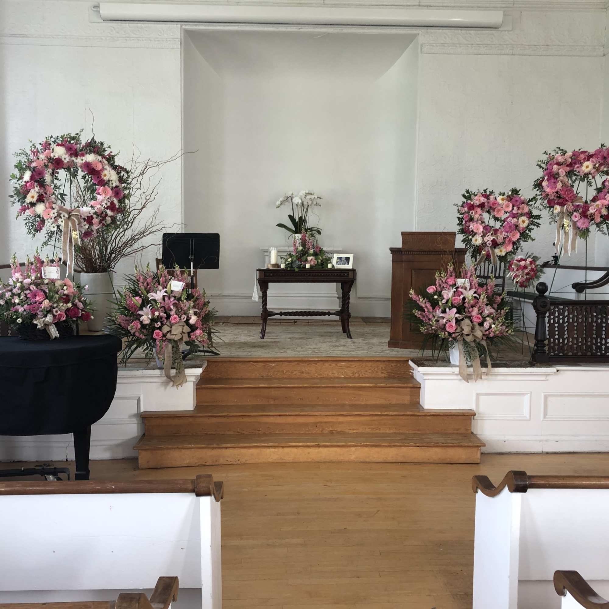 Pink floral wreaths and arrangements displayed on a church stage