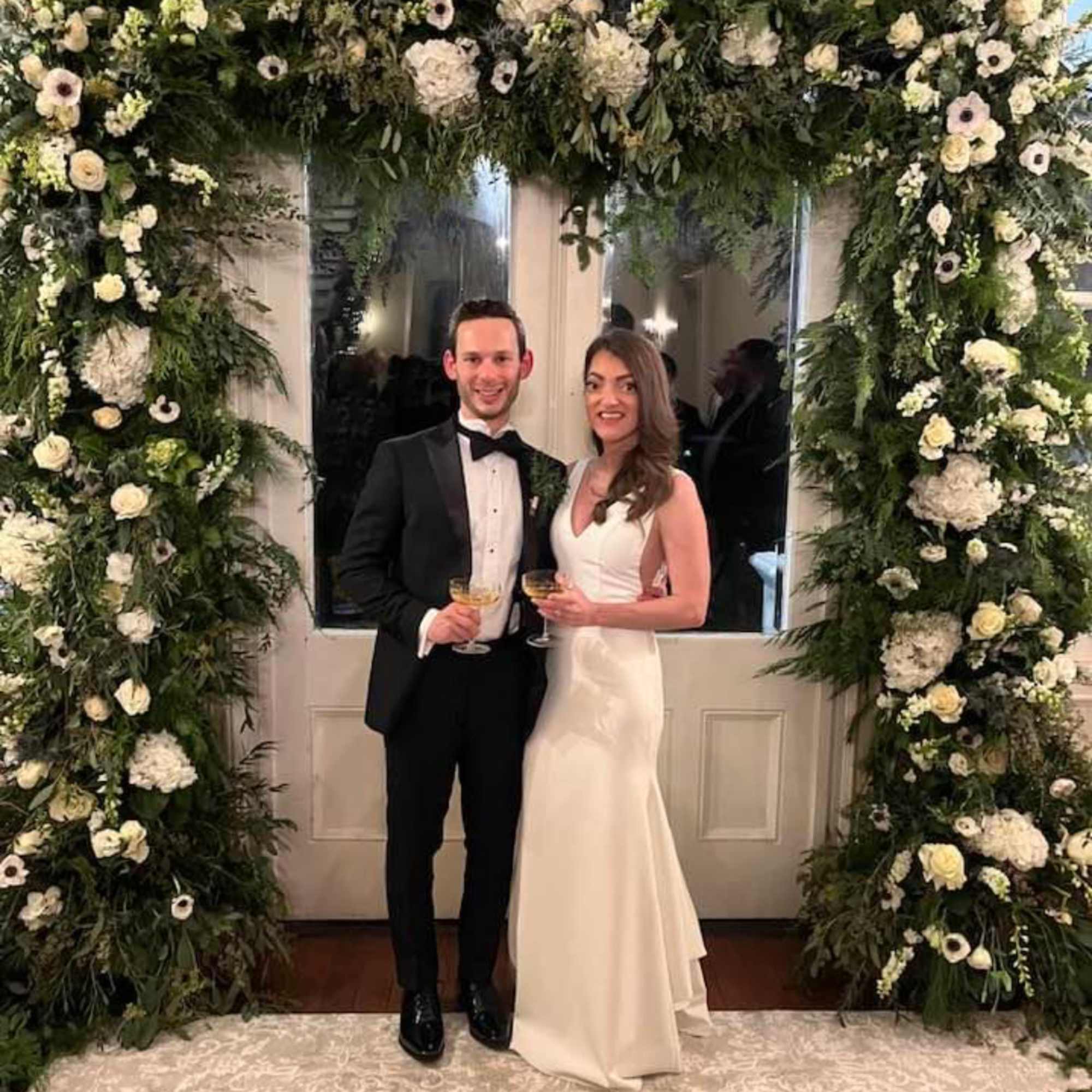 Large white floral arch framing a couple in formal attire