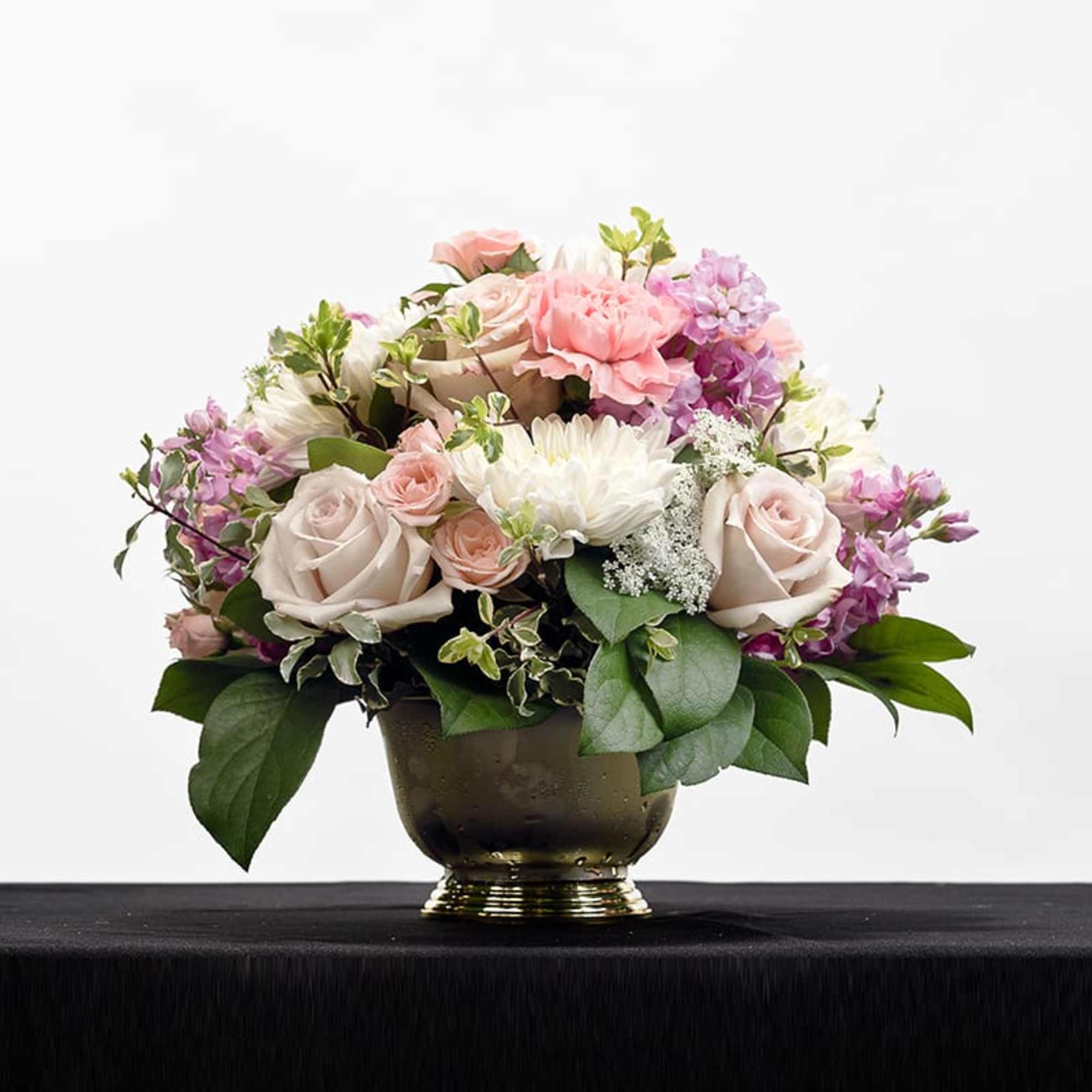 Low arrangement of pale pink roses, carnations and white mums in a gold pedestal bowl