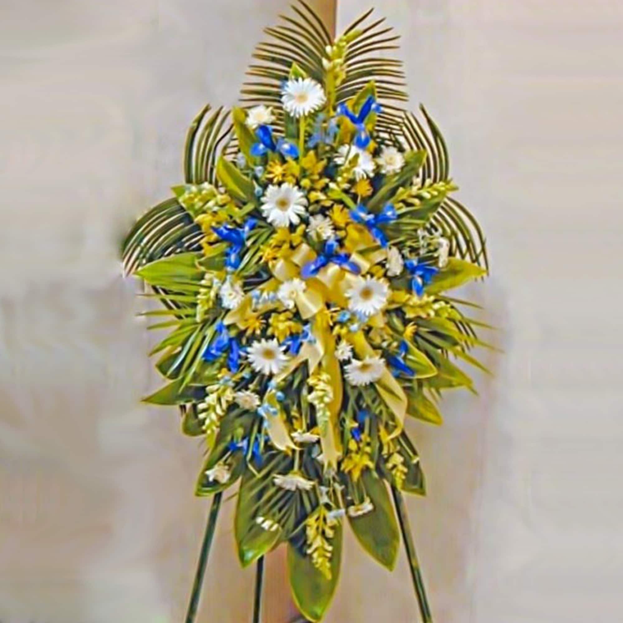 Tall standing spray with white daisies and blue and yellow flowers on a fan of large green leaves