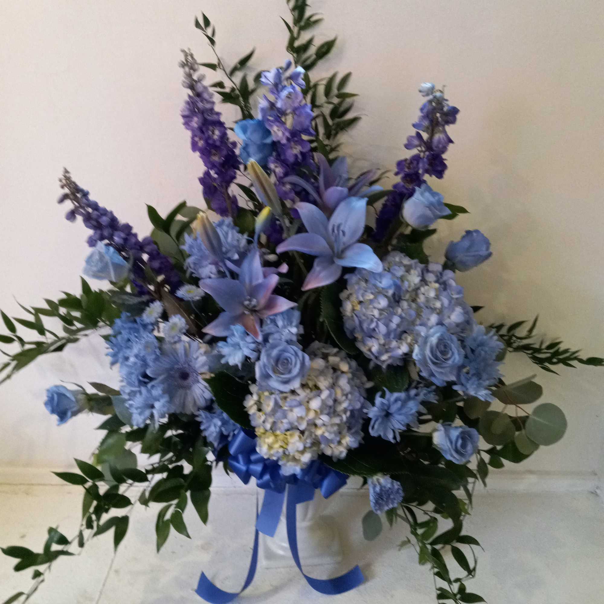 Blue and purple floral arrangement in a white container with a ribbon