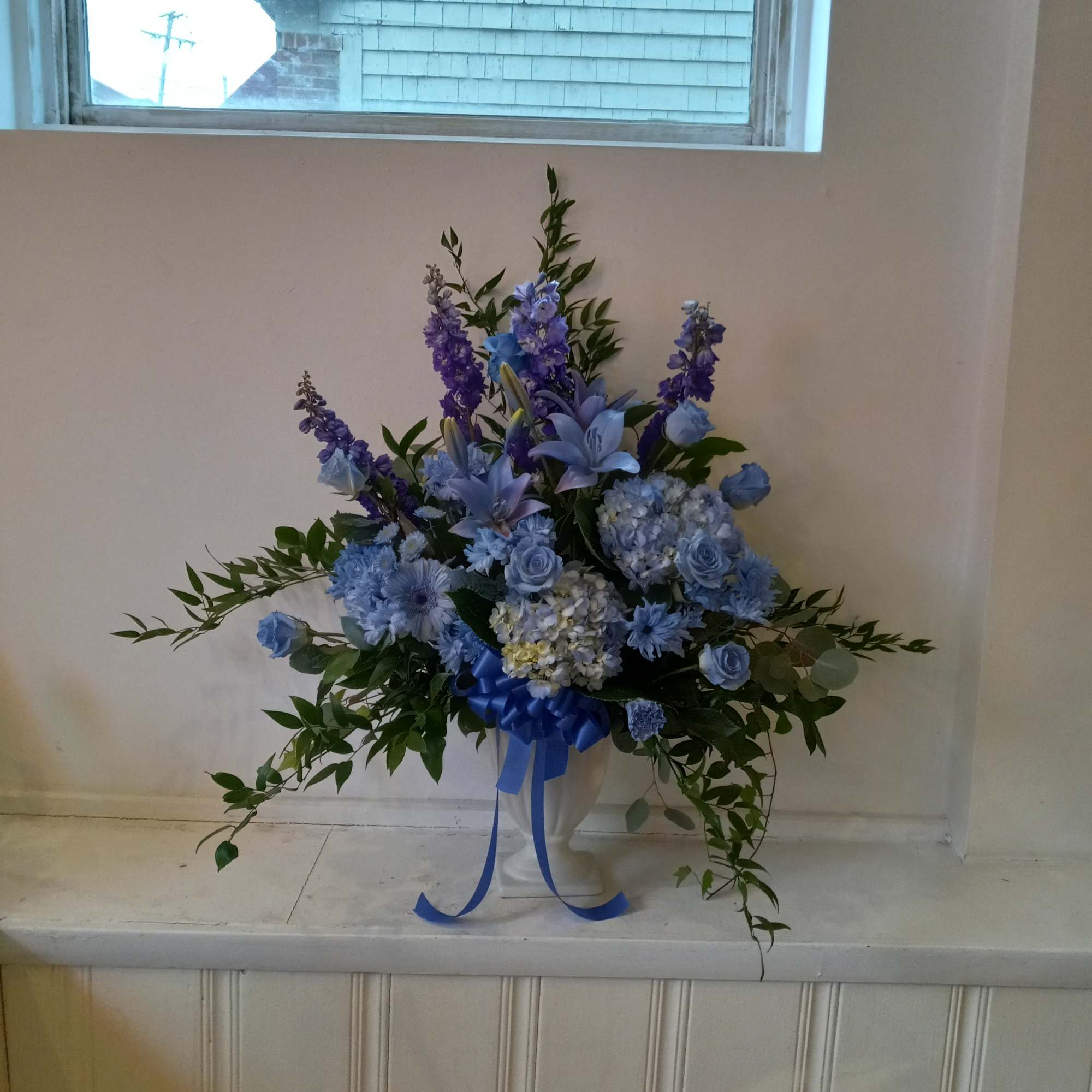 Blue floral arrangement in a white urn with a ribbon