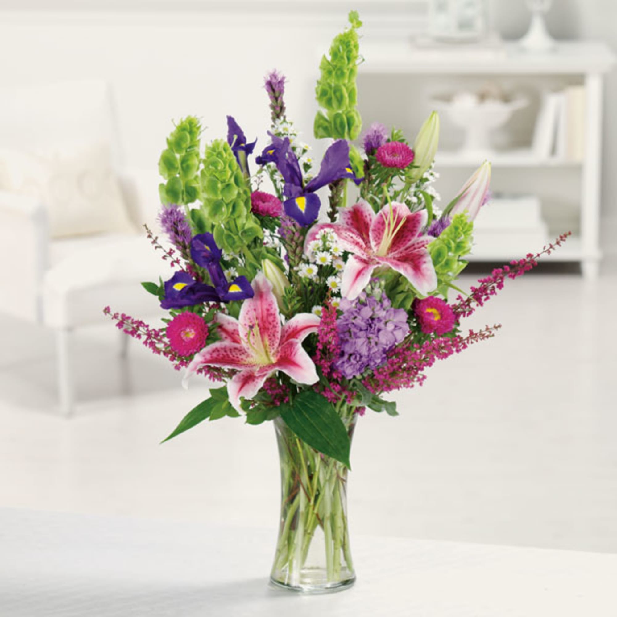 Mixed bouquet of pink lilies, purple irises, and green spikes in a glass vase