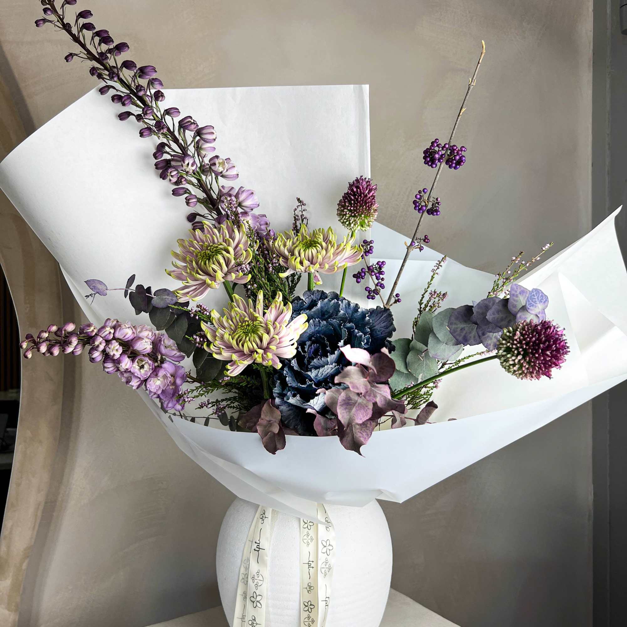 Purple and green bouquet in a white vase with paper wrap