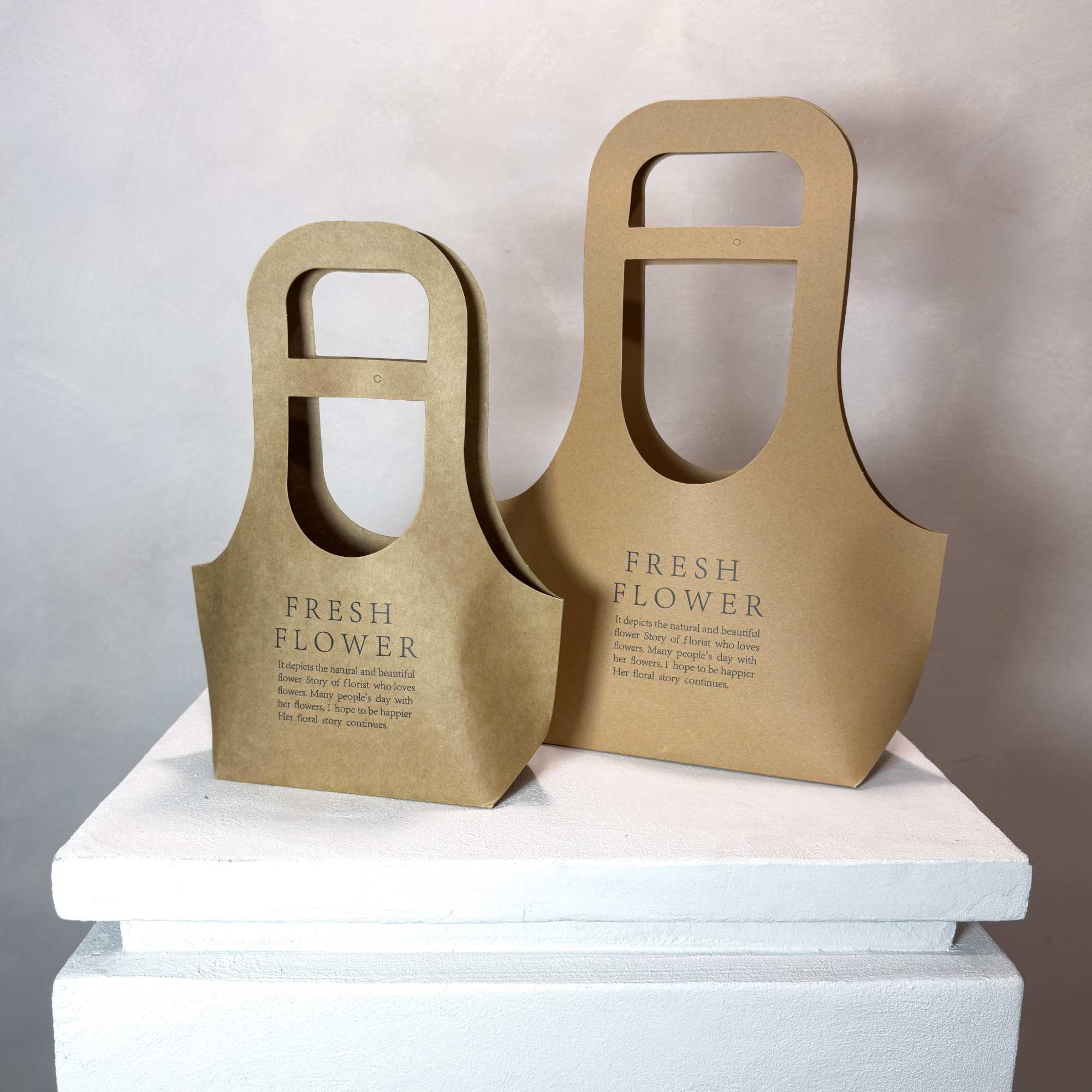 Two brown paper flower carriers with cutout handles on a white surface.