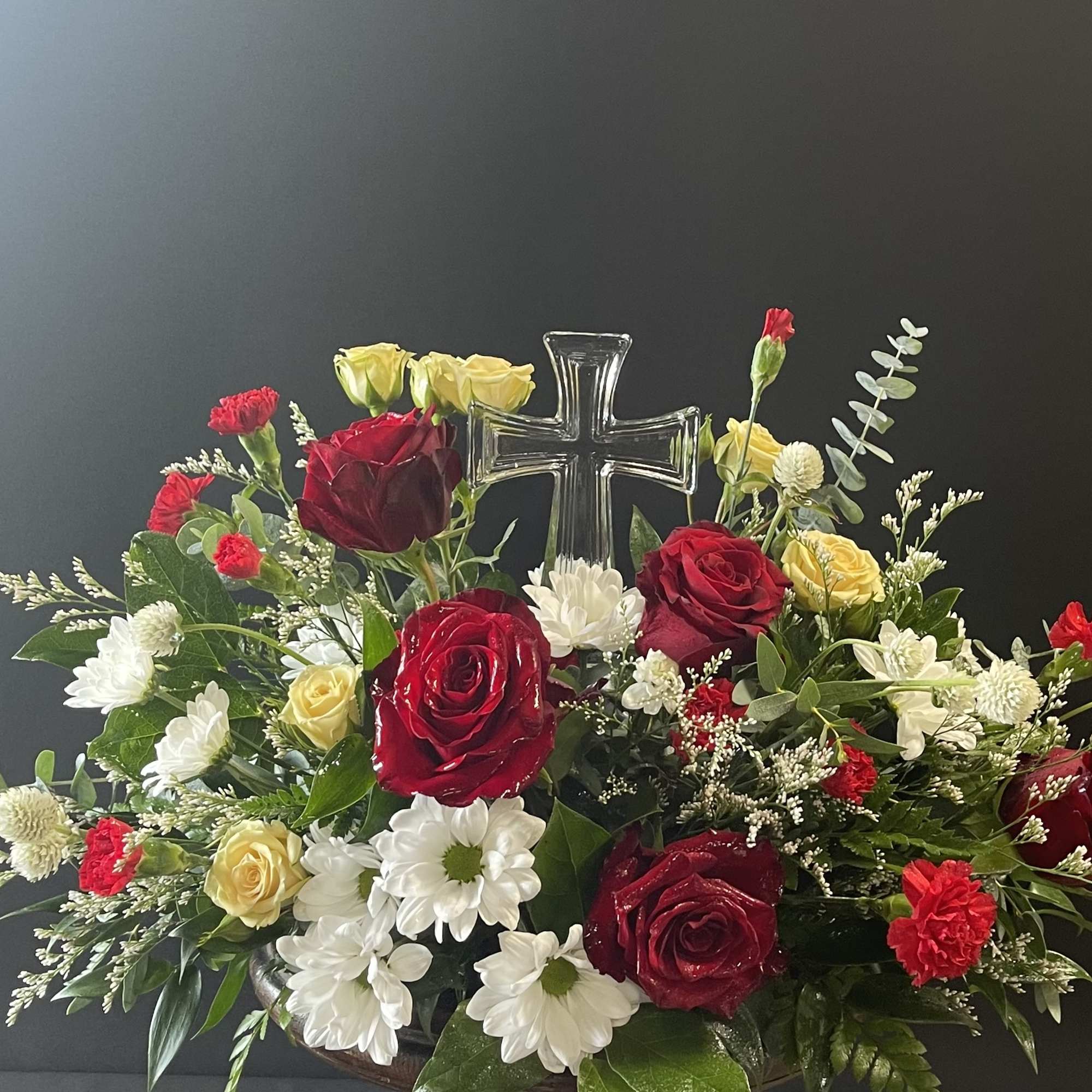 Red and yellow roses with white daisies around a clear cross