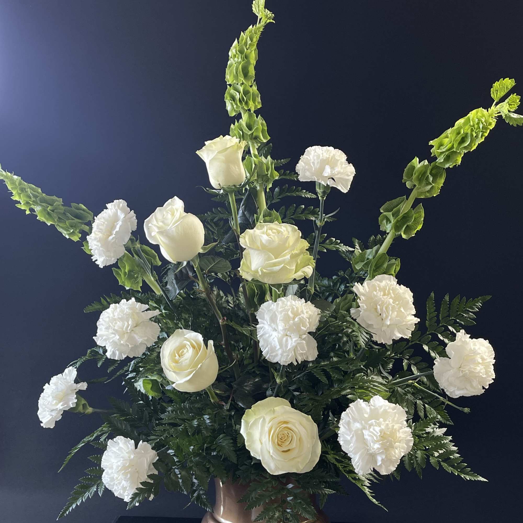 White roses and carnations in a bronze vase with tall green spikes