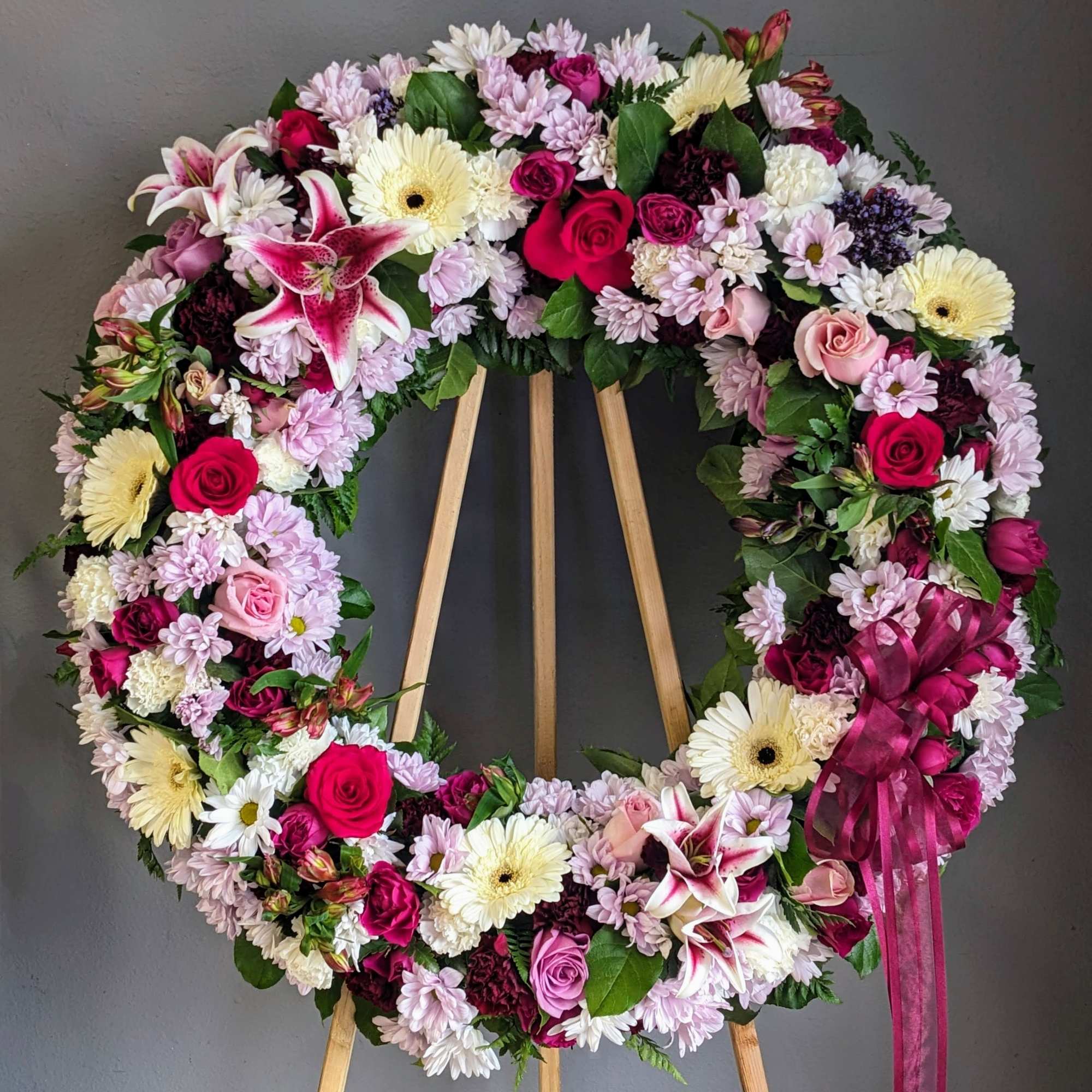 Large pink and white floral wreath on a wooden easel with a ribbon bow